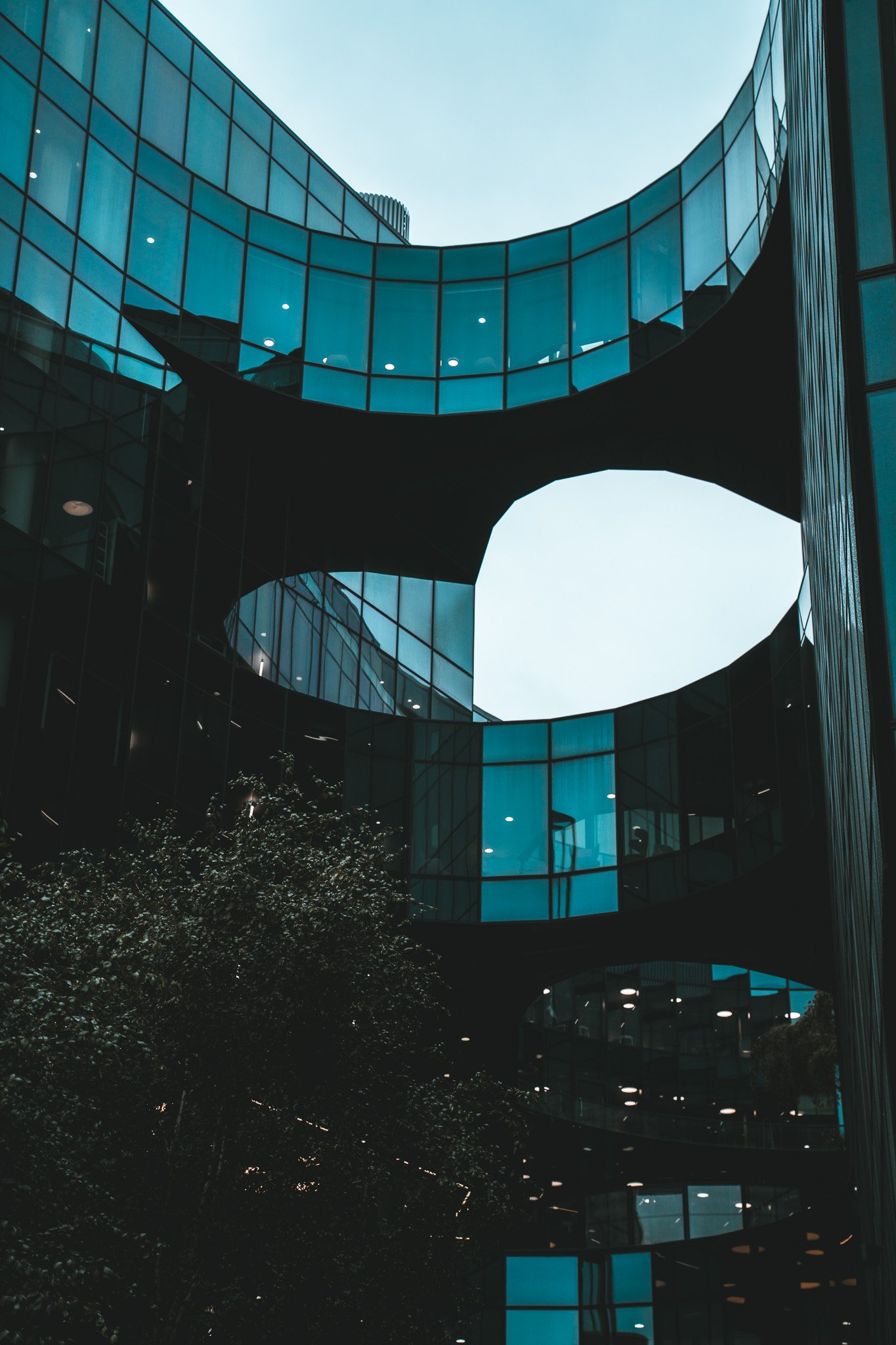 Modern building with glass facades and curved architectural design, featuring large openings and illuminated interior lights.