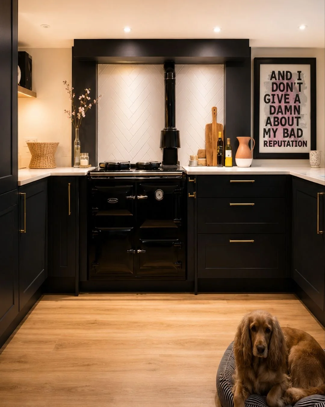 Dark cottage kitchen with inherited Rayburn range cooker, herringbone white tile splashback, matt black shaker cabinets and bold typography artwork, Suffolk interior design
