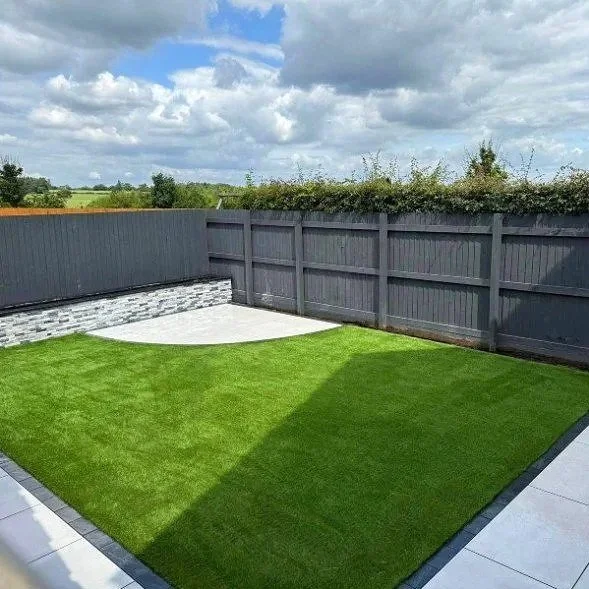A backyard with a well-maintained green lawn, grey privacy fence, corner paved area, and cloudy sky overhead.