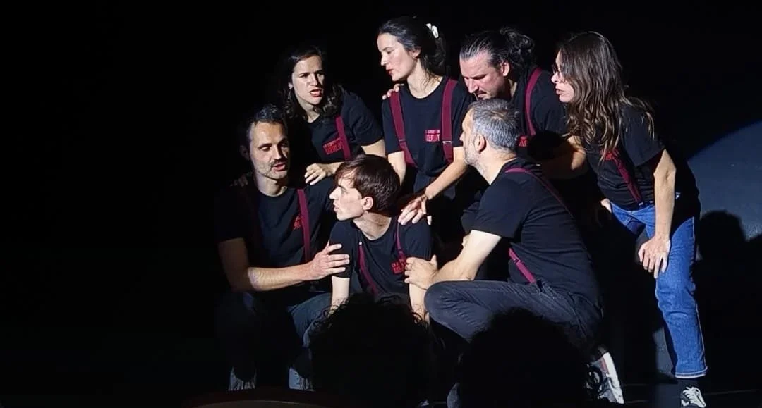 Groupe de personnes en théâtre pendant une performance, portant des t-shirts noirs avec des détails rouges, dans une scène sombre.