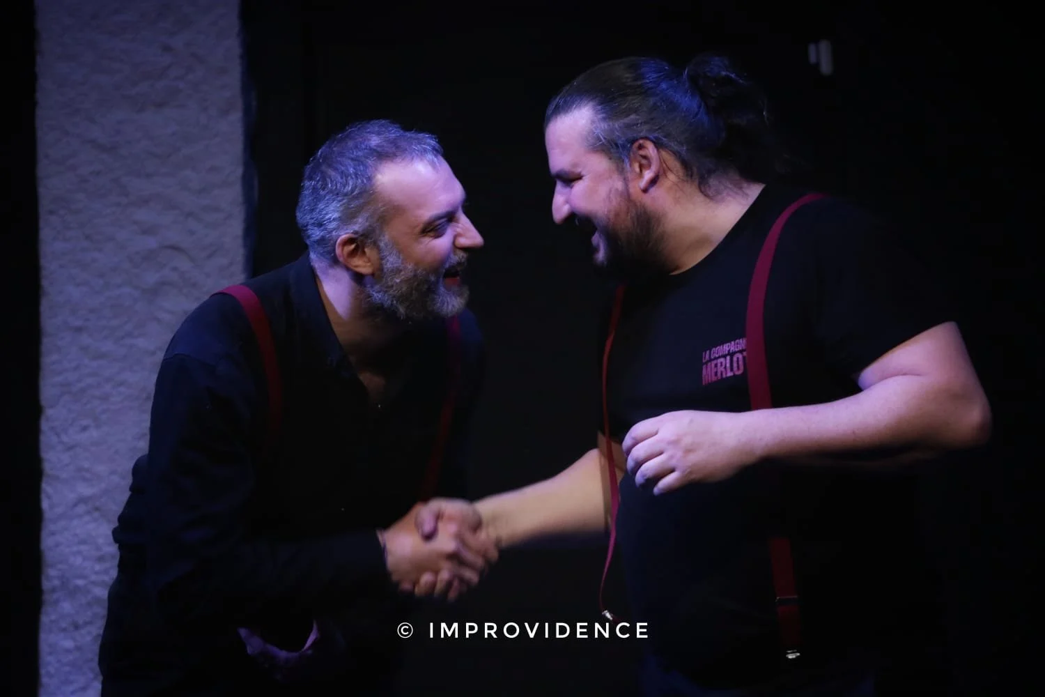 Deux hommes se serrent la main, se sourient et semblent heureux dans une scène de spectacle ou de spectacle humoristique.