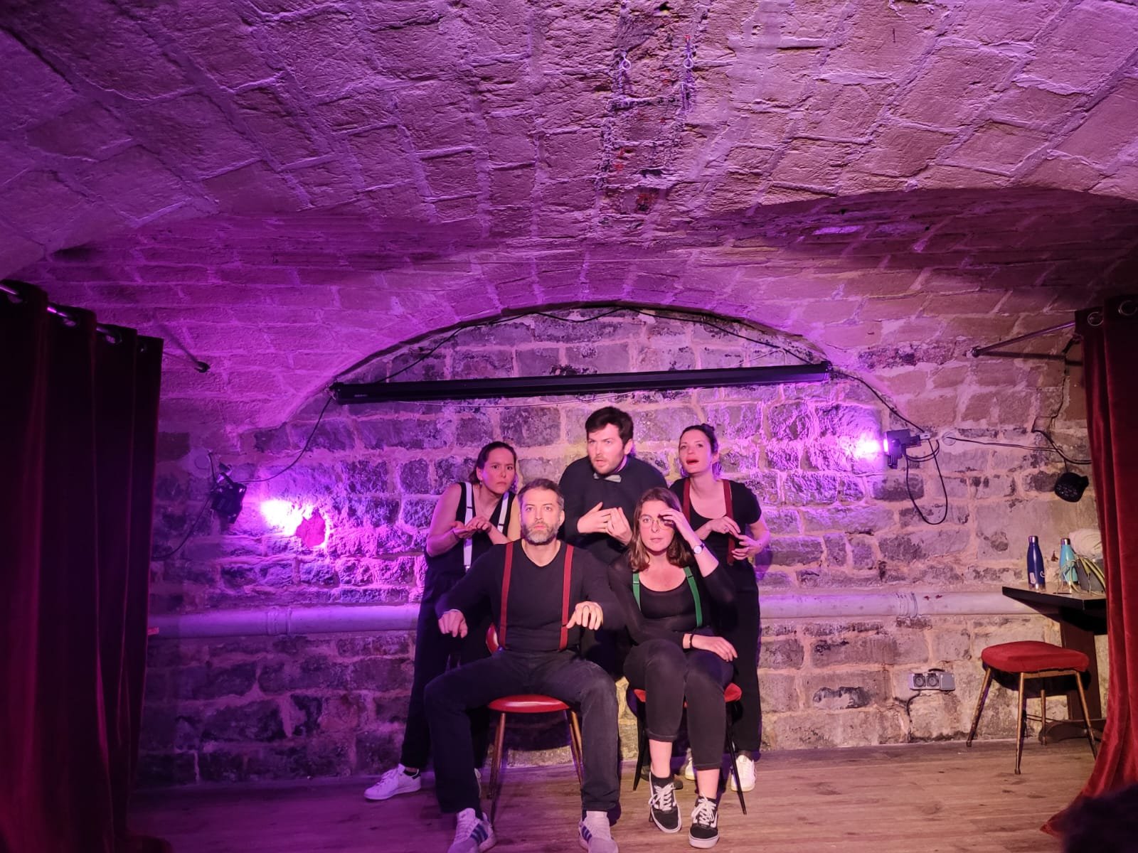 Groupe de cinq personnes en costume noir se produisant sur un petit théâtre en pierre, avec éclairage violet.