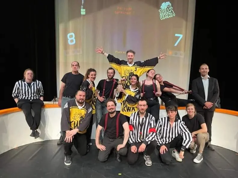 Groupe de personnes posant sur scène, certains portant des maillots de hockey jaunes, avec un décor de jeu télévisé en arrière-plan.