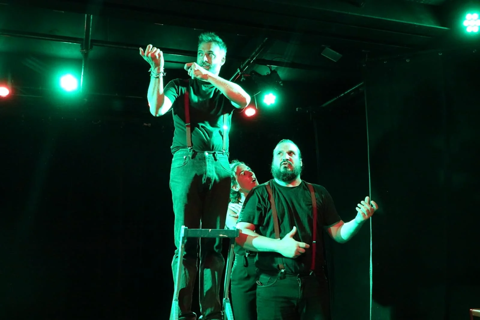 Trois personnes sur une scène, deux debout et une assise, avec des lumières vertes et rouges