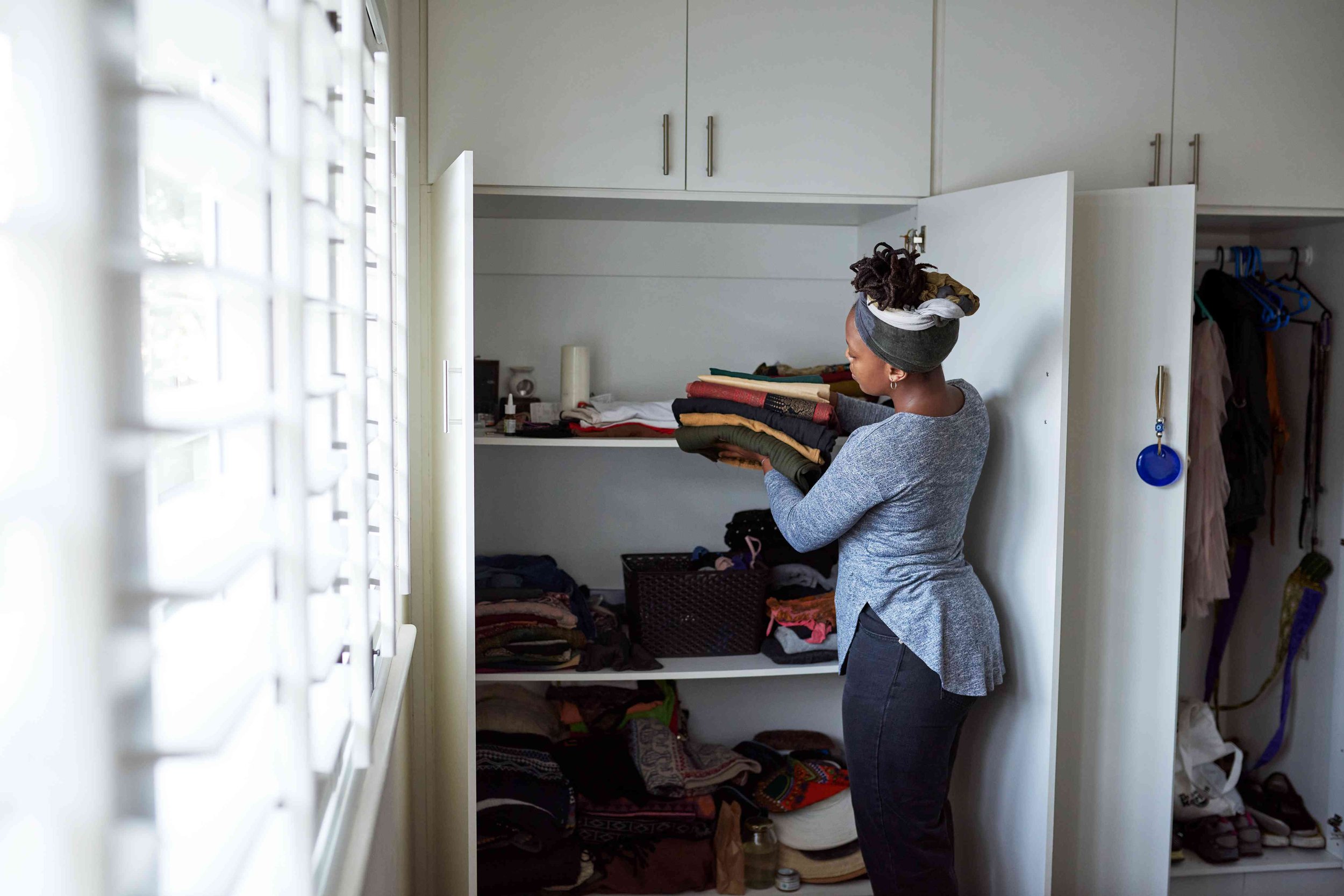 Woman organizing folded clothes in a closet near a window
