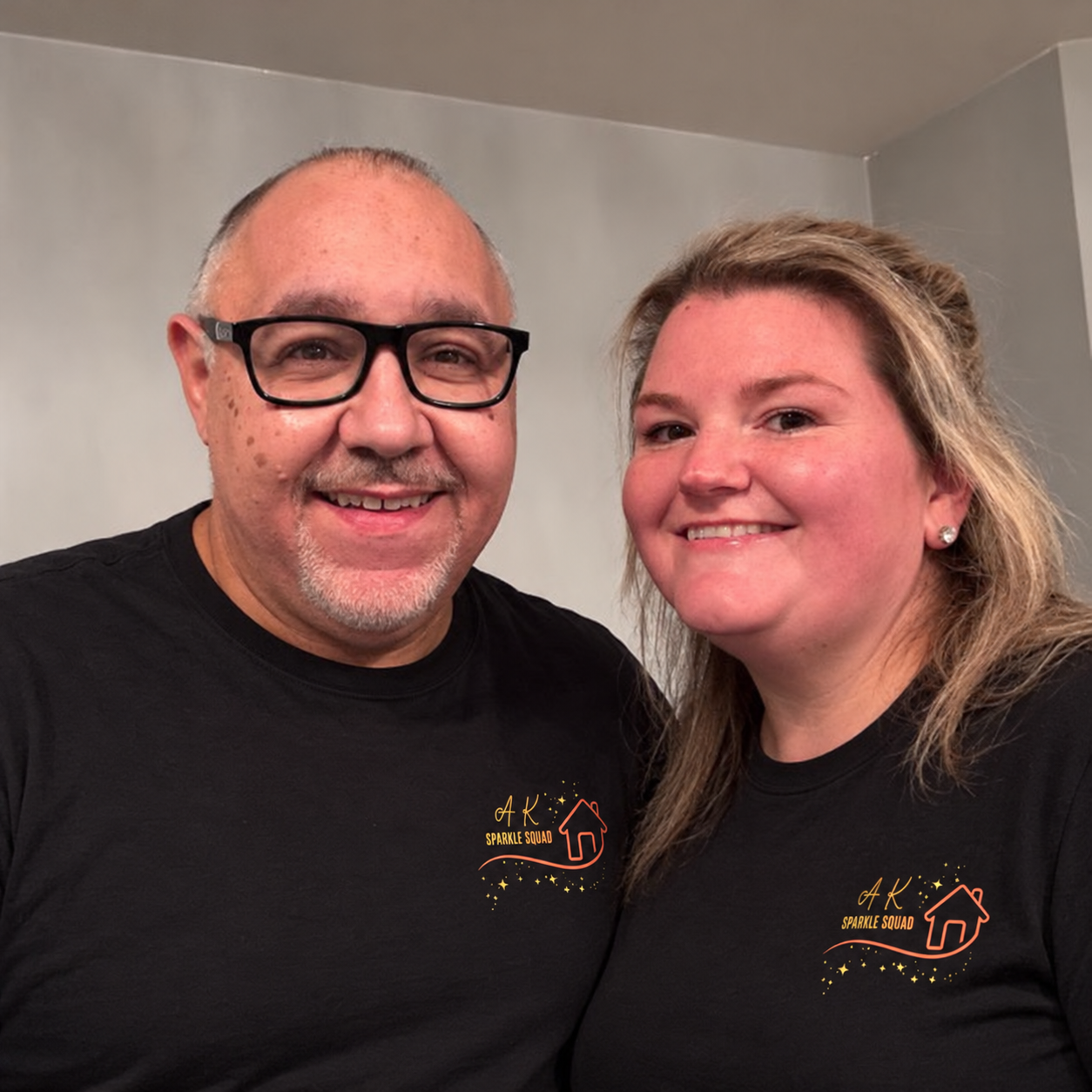 Smiling man and woman wearing matching black AK Sparkle Squad shirts