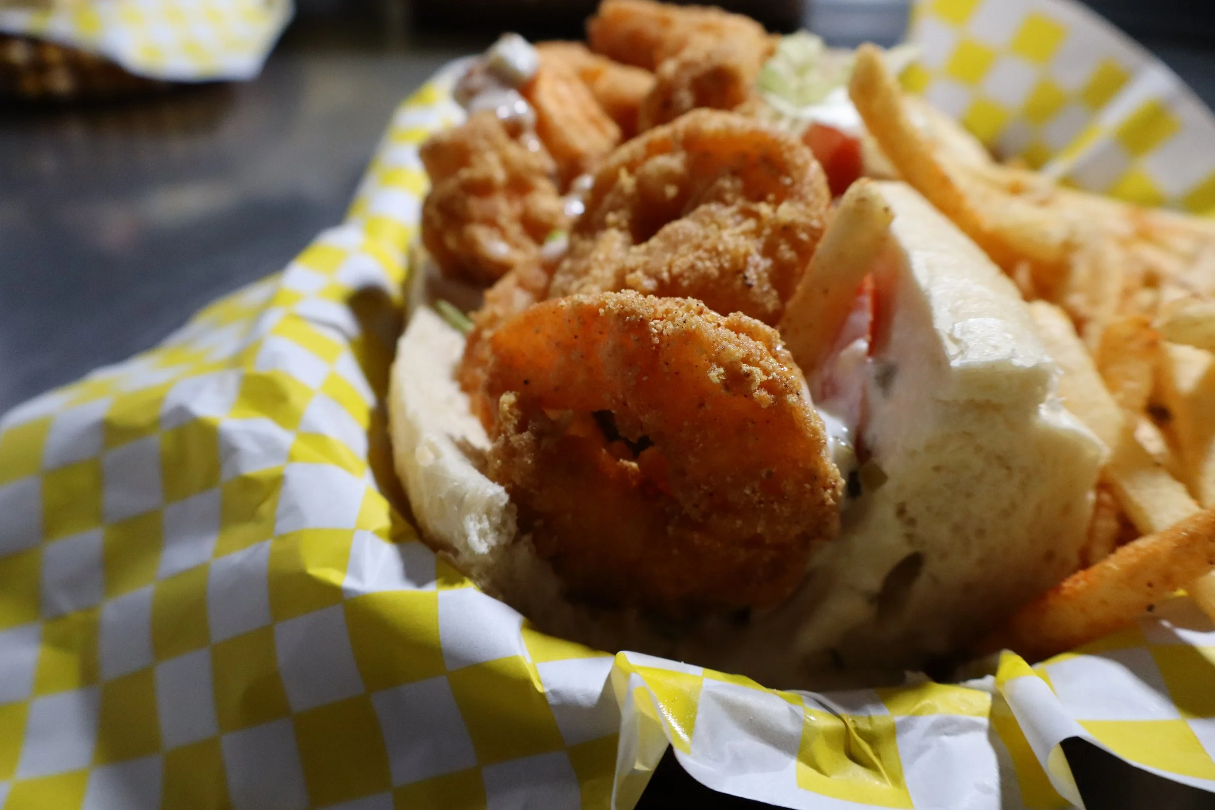 Fried seafood platter with crab cakes, French fries, and coleslaw in a yellow checkered paper basket.