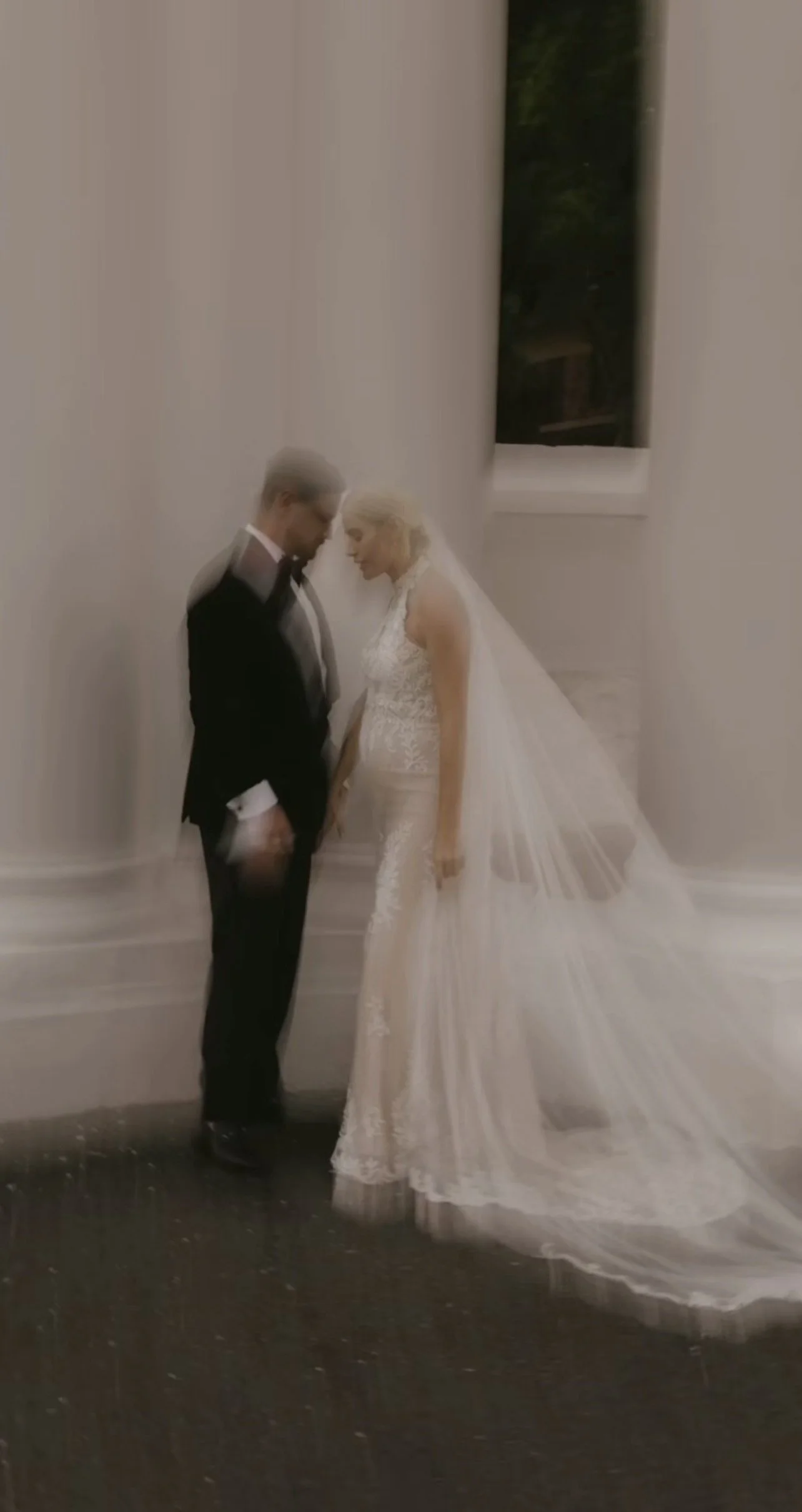 A bride and groom sharing an intimate moment indoors at their wedding, standing close to each other with foreheads touching.