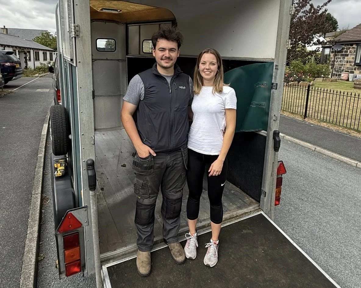 A man and a woman standing inside the back of a moving truck, smiling at the camera.