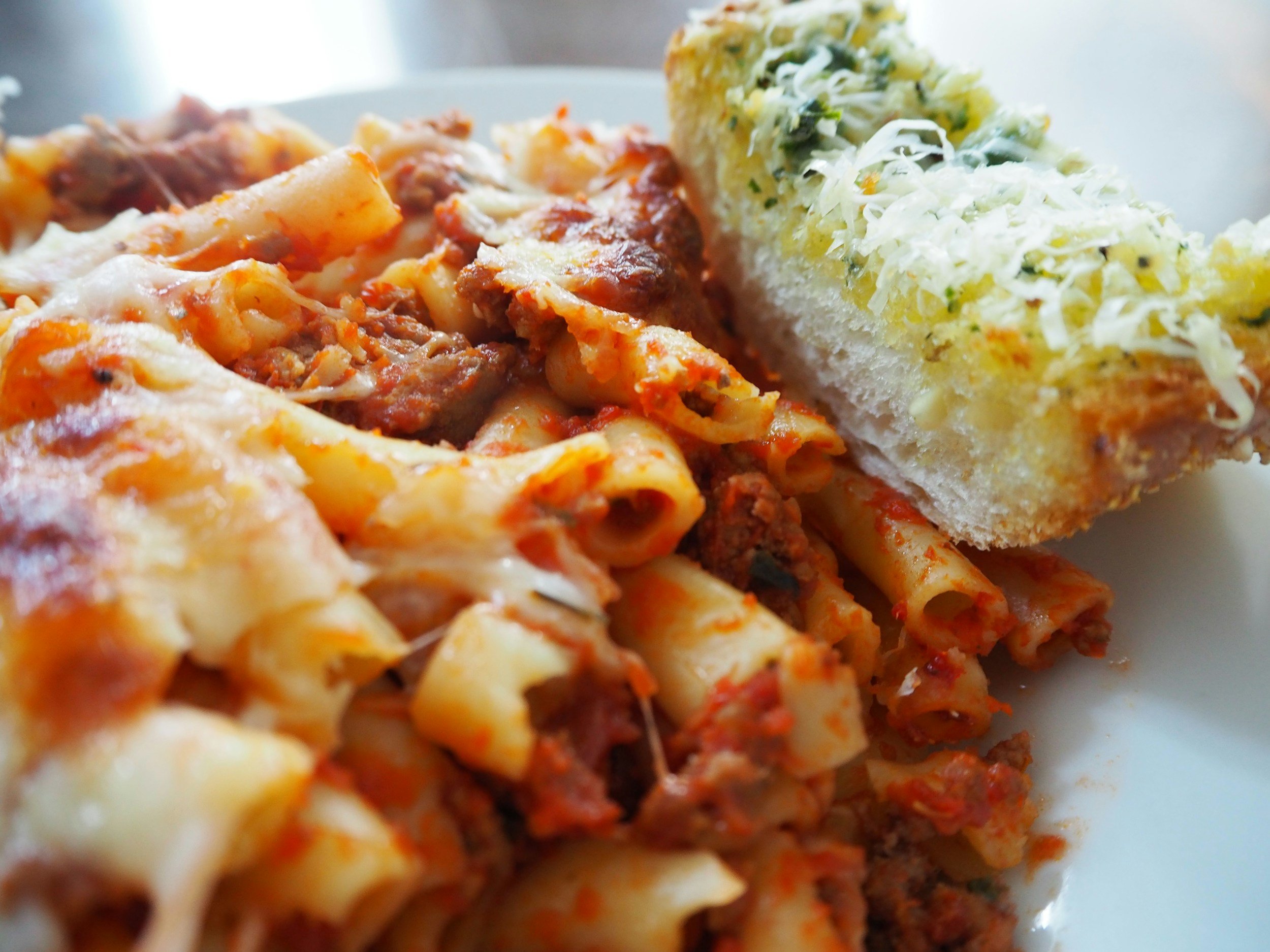 Close-up of cooked pasta with meat sauce and a piece of garlic bread topped with cheese and herbs.