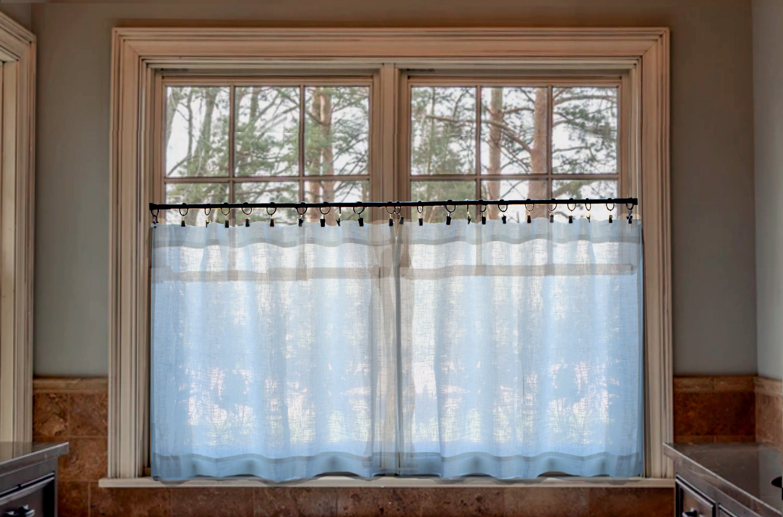 Window with wooden trim and light blue sheer curtains, view of trees outside.