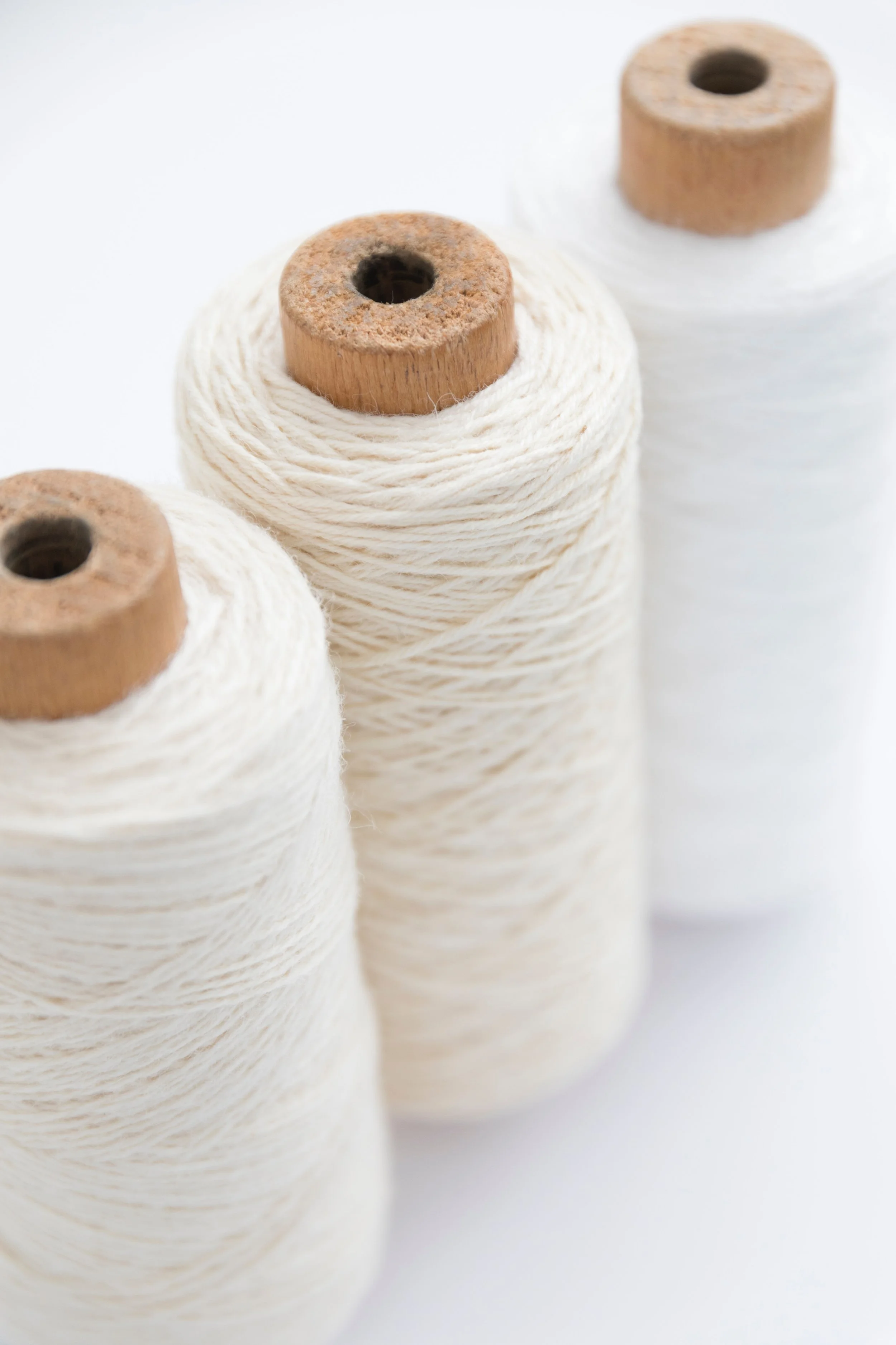 Three spools of white thread with wooden cores on a white background.
