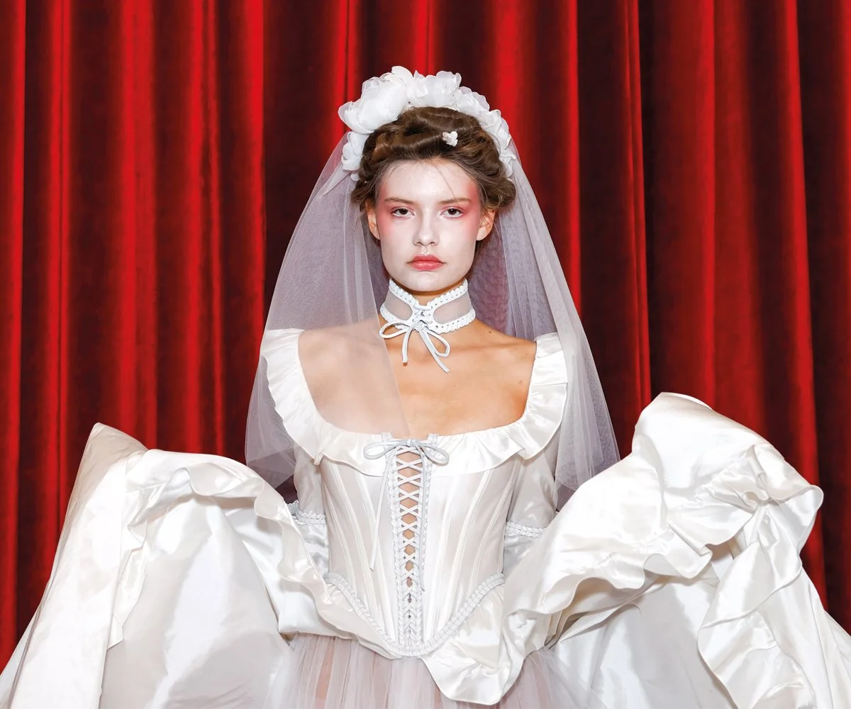 Behind-the-scenes fashion photography of a model backstage during hair and makeup before a runway show.