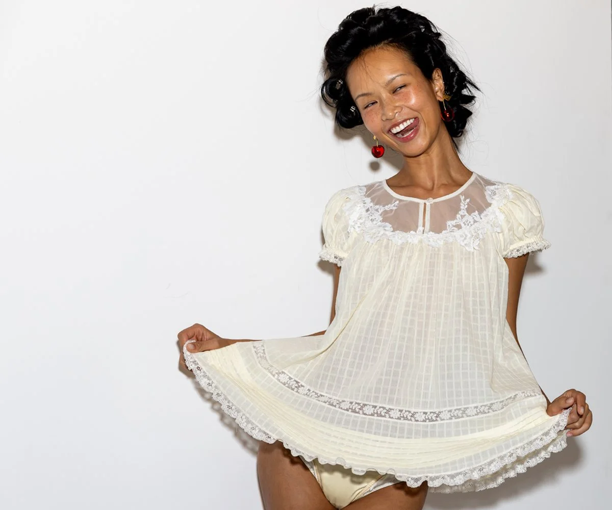 Model backstage at London Fashion Week smiling in a white lace dress during final preparations