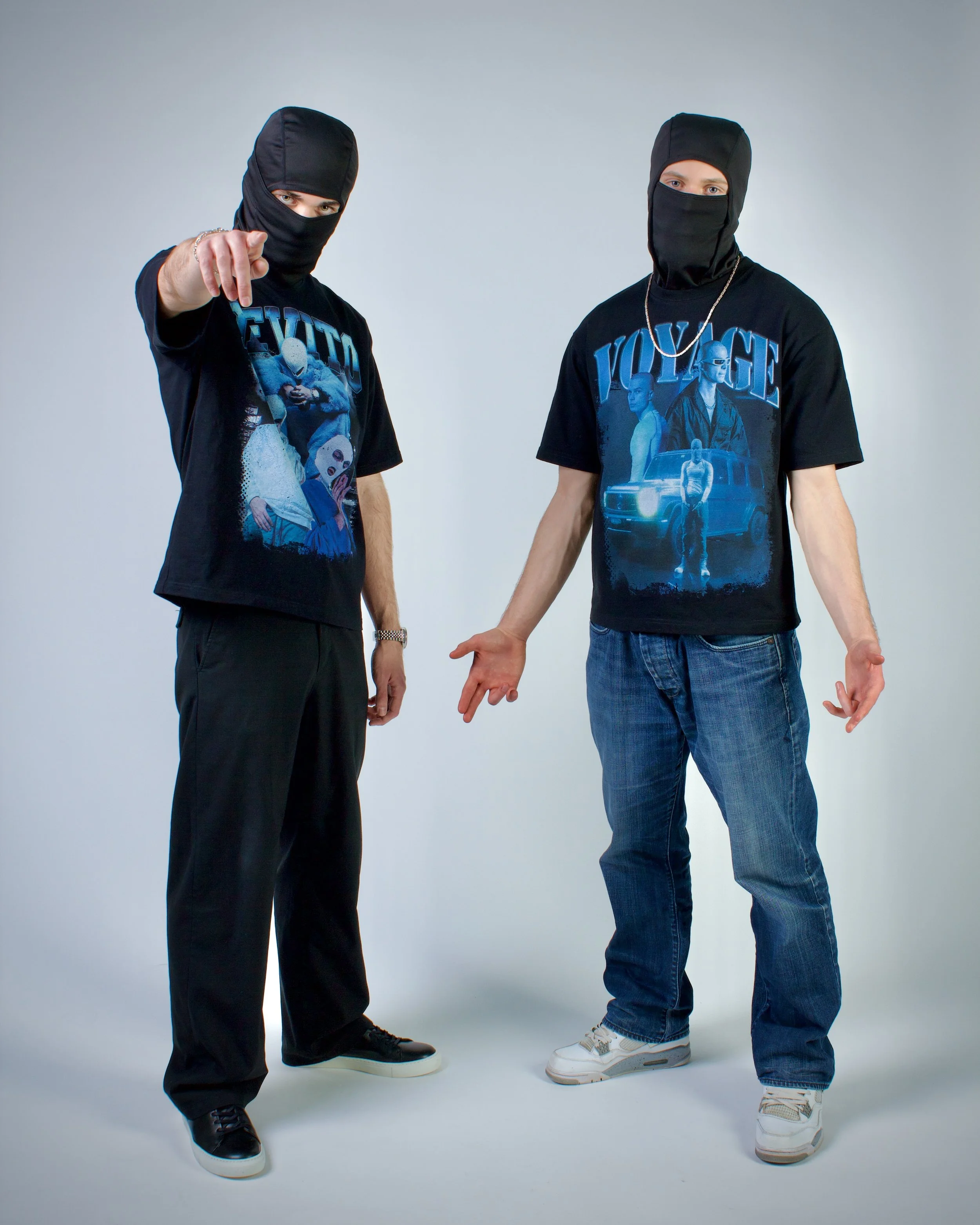 Två personer i svarta maskeringar, t-shirts med grafiska motiv, ett pekar mot kameran, den andra står med öppna händer.