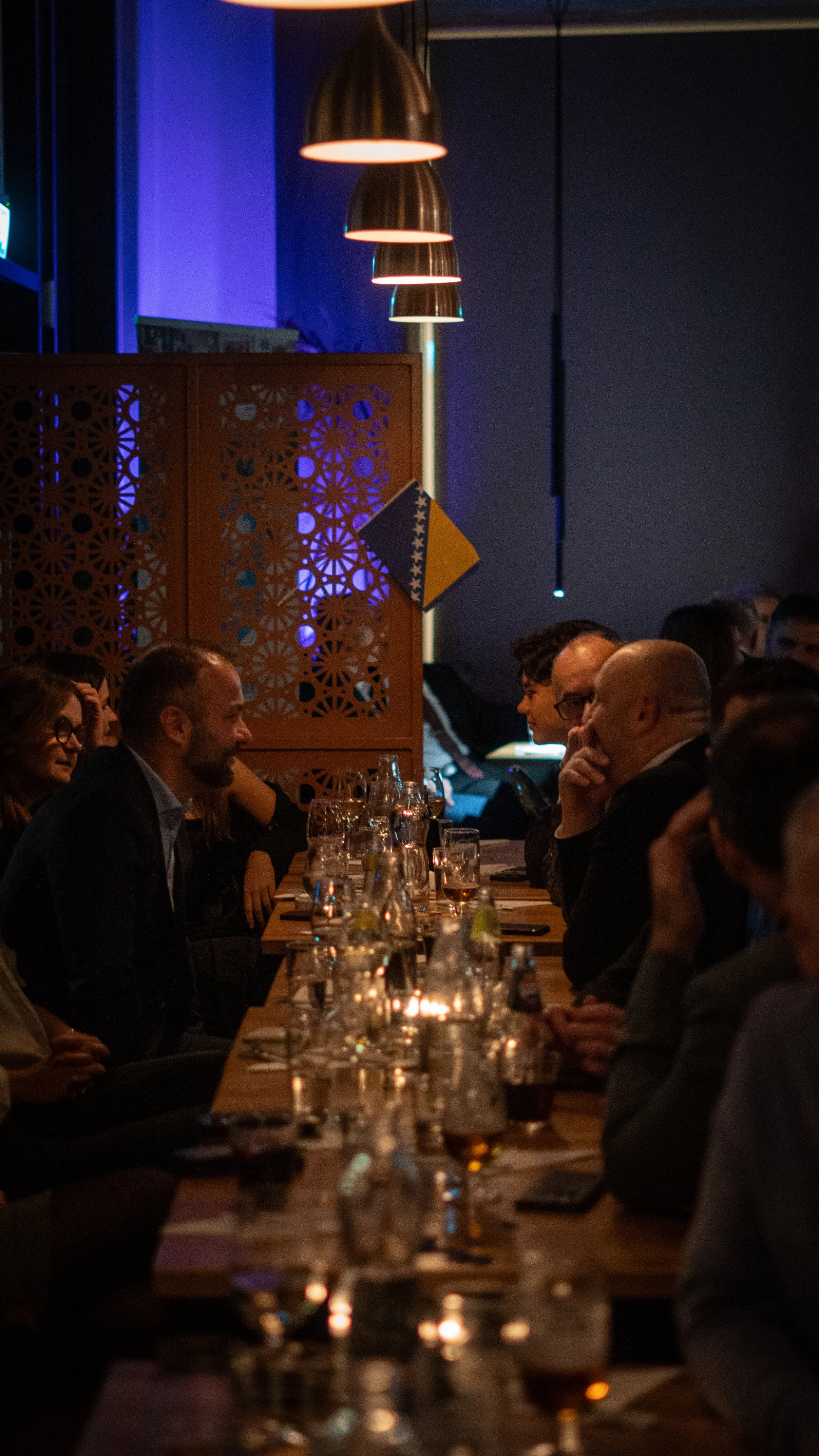 Människor samlade runt ett bord i ett mörkt rum, med öl och glas. Svenskt och bosniskt flagg i bakgrunden.