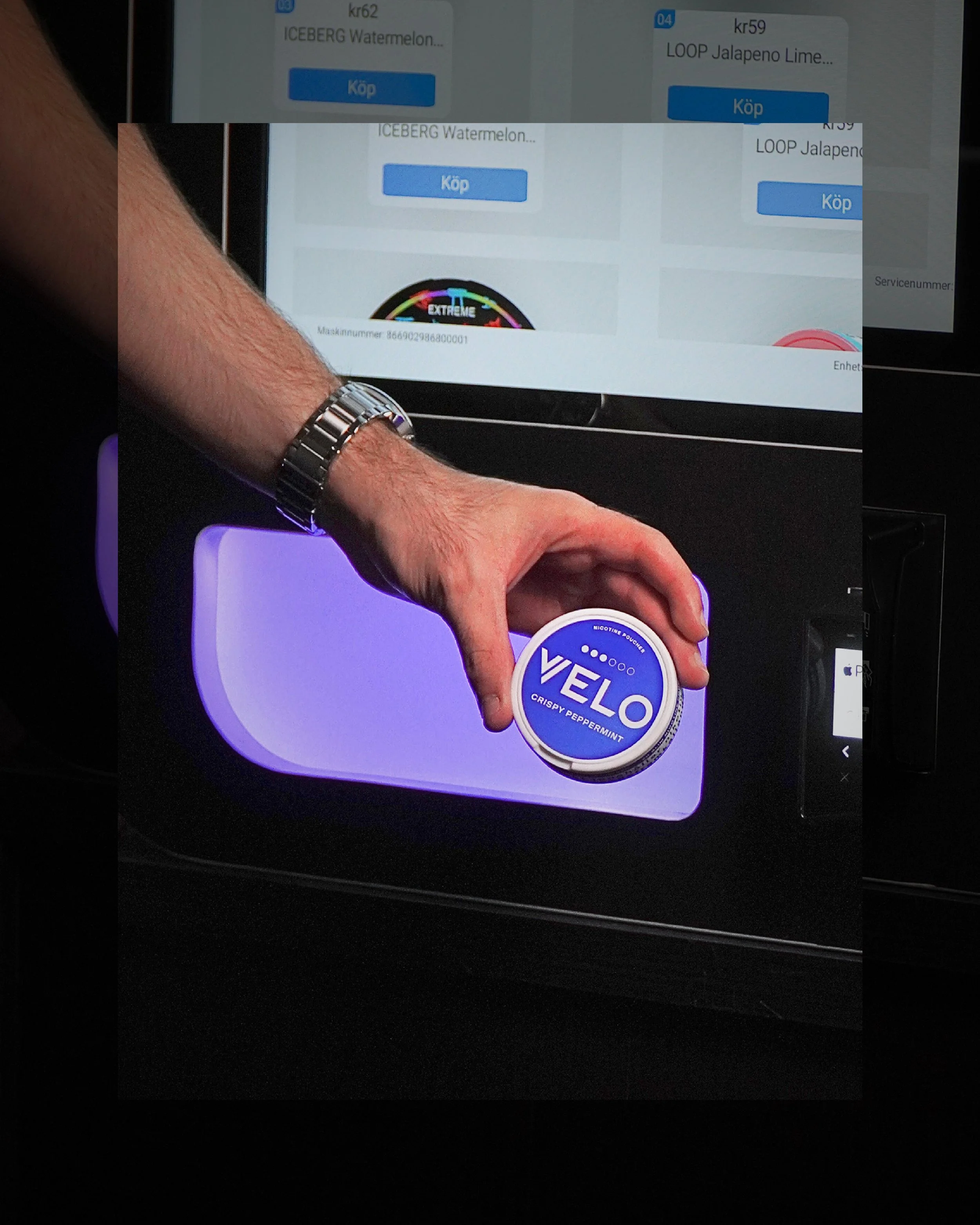 En person håller ett snusburk med märket VELO CREAM PEPPERMINT framför en digital kiosk.