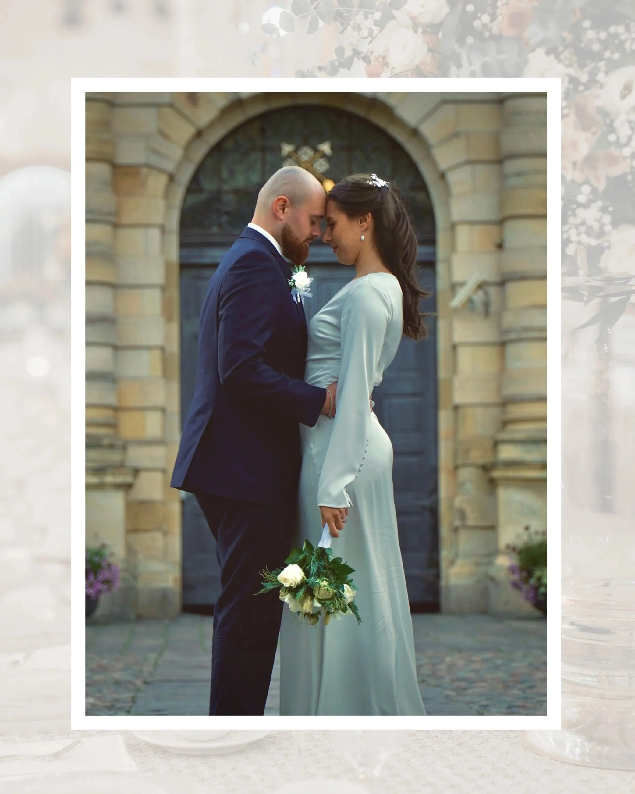 Ett brudpar står nära varandra med pannan mot pannan framför en gammal tegelbyggnad.