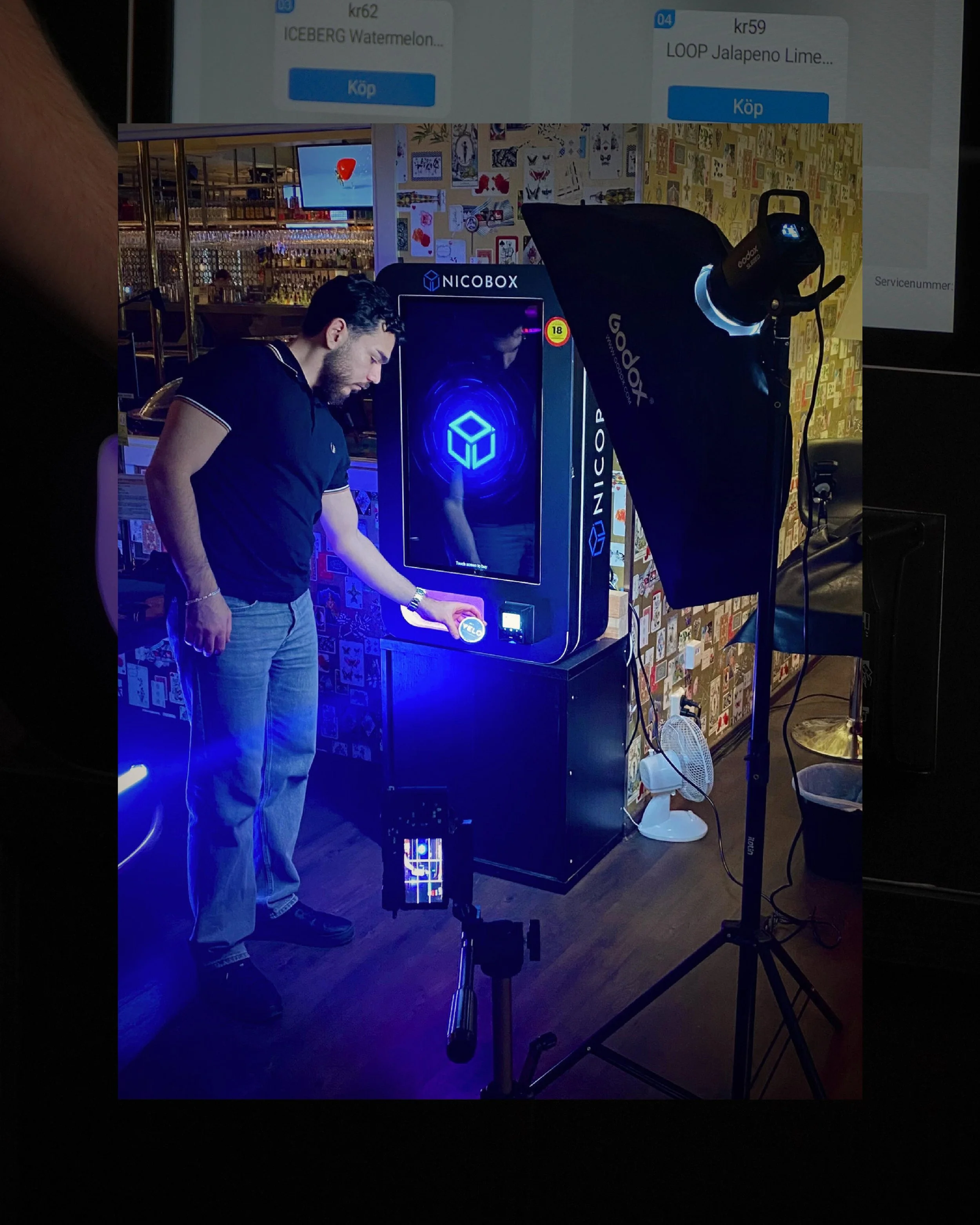 En man använder en futuristisk maskin med responsiv skärm i en mörk miljö, med fotografi- och dekorationsmaterial på väggarna bakom.