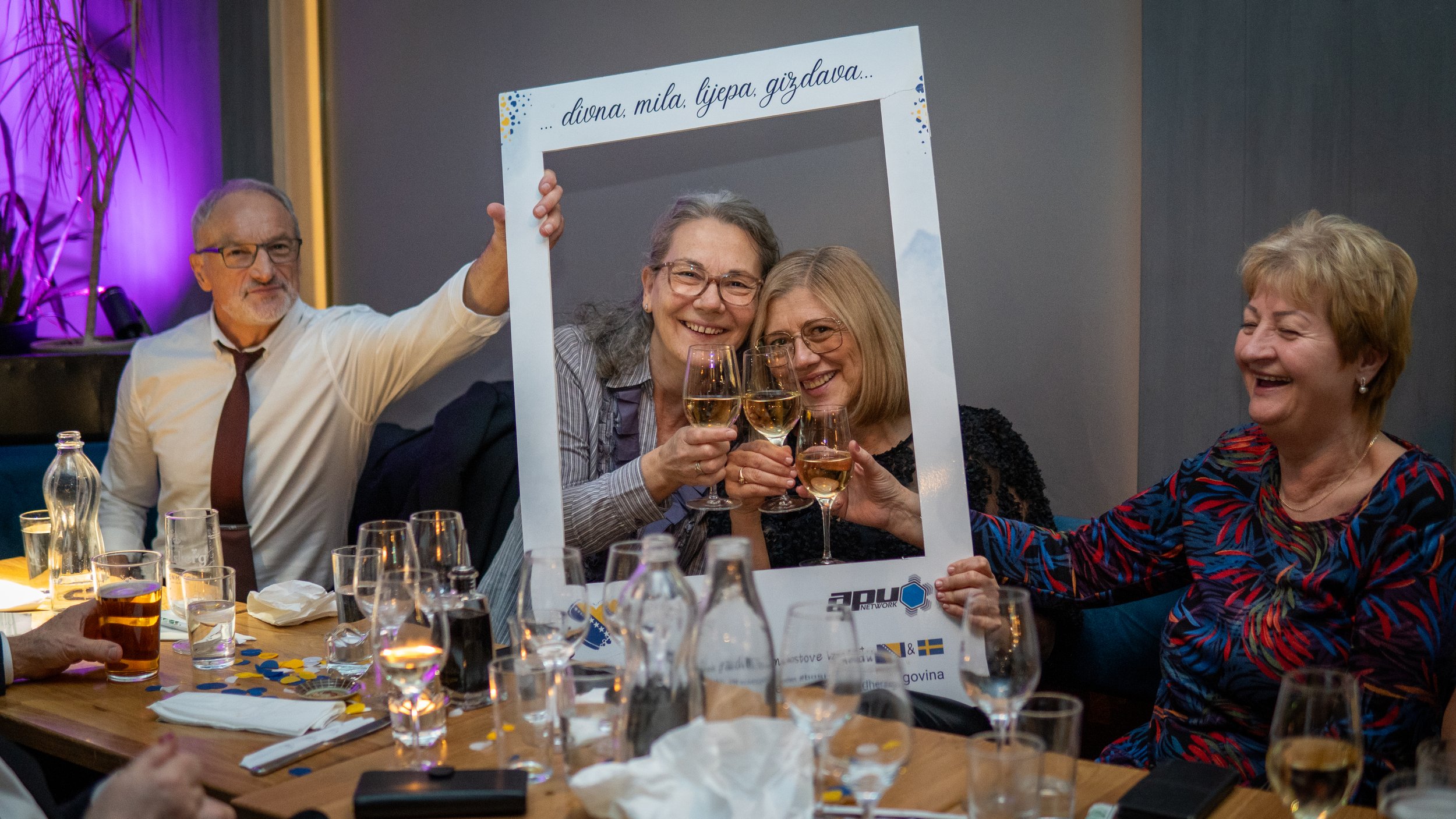 Fyra personer elev att skåla med vin i ett festligt sällskap, omges av glas och dekorationer.