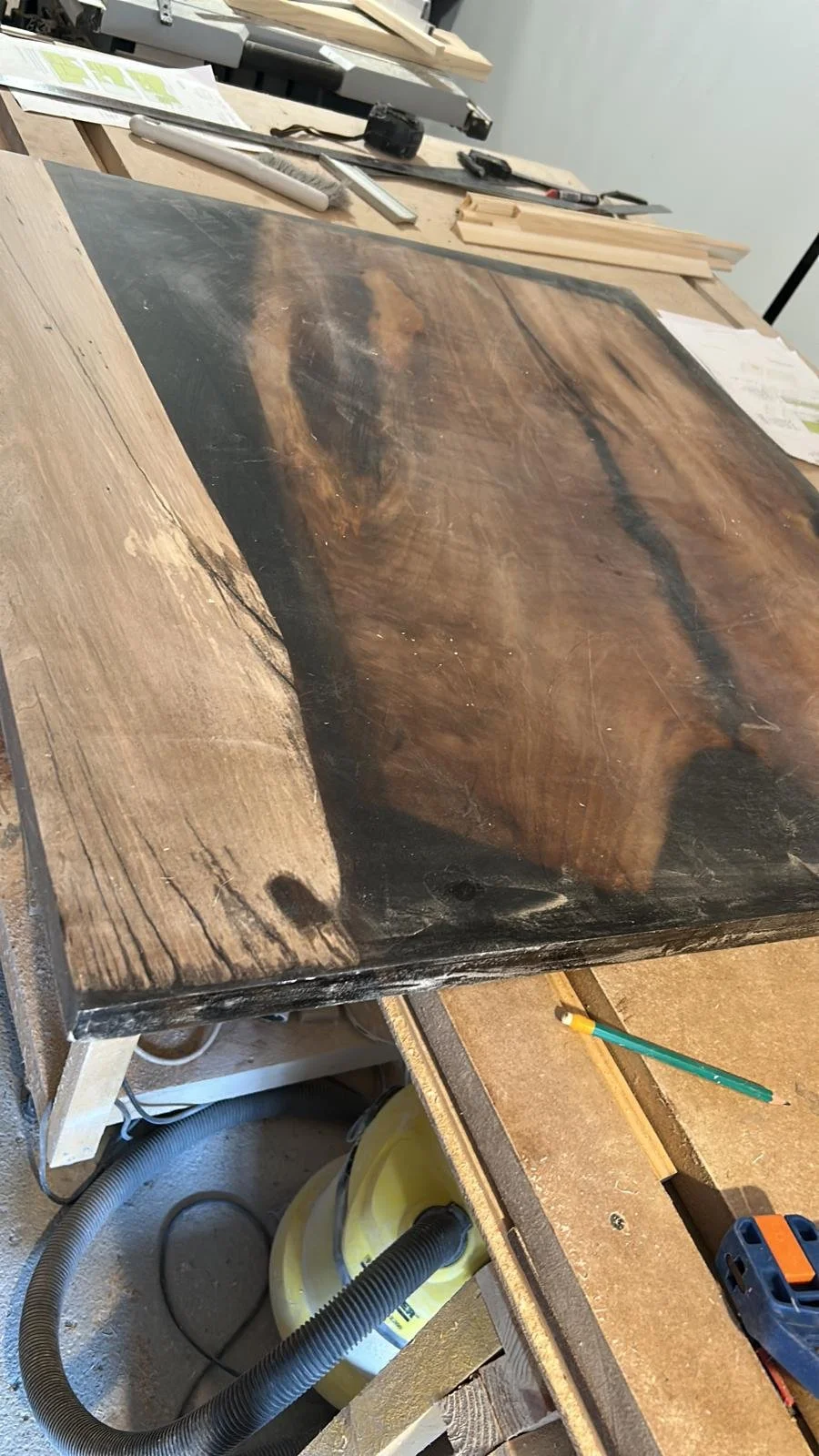 Table en bois avec un mélange de bois clair et foncé, dans un atelier de menuiserie, avec des outils et des matériaux visibles.