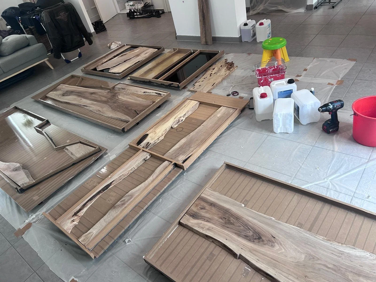 Planches de bois en cours de fabrication ou de finition, posées sur une surface couverte de papier ou plastique, avec des outils et des contenants de liquide à proximité.