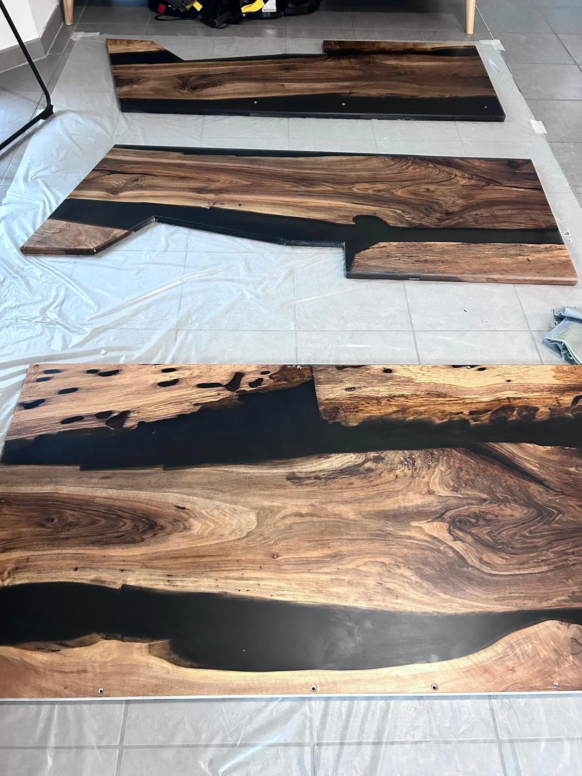 Trois grandes planches de bois avec des accents en résine, disposées sur un sol carrelé pour un projet de fabrication de meubles.