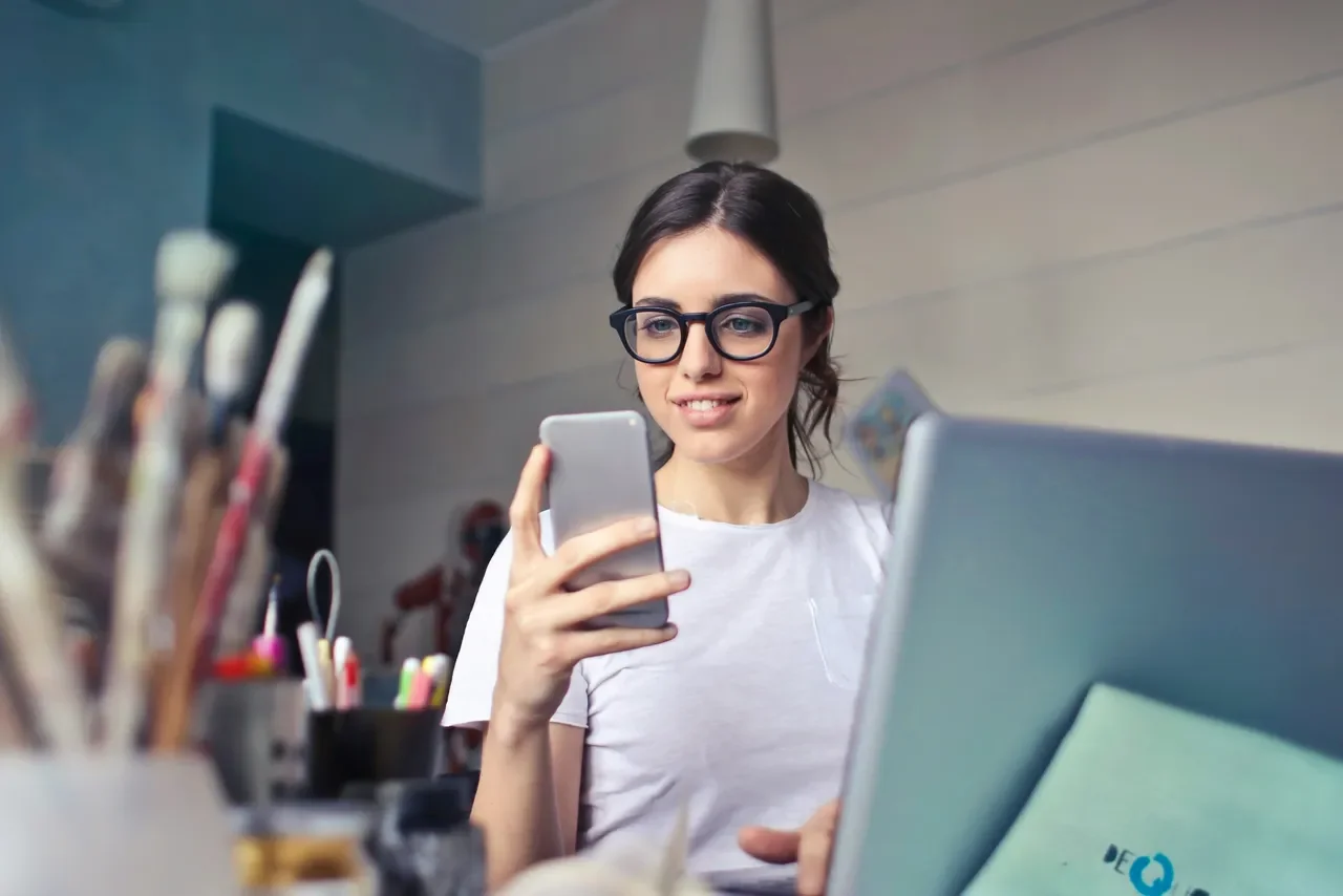 Woman reviewing marketing information on phone and laptop, representing online marketing clarity in 2026 without noise.