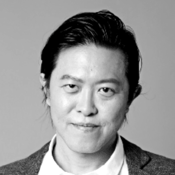 Black and white portrait of a man in a blazer and collared shirt, smiling slightly.