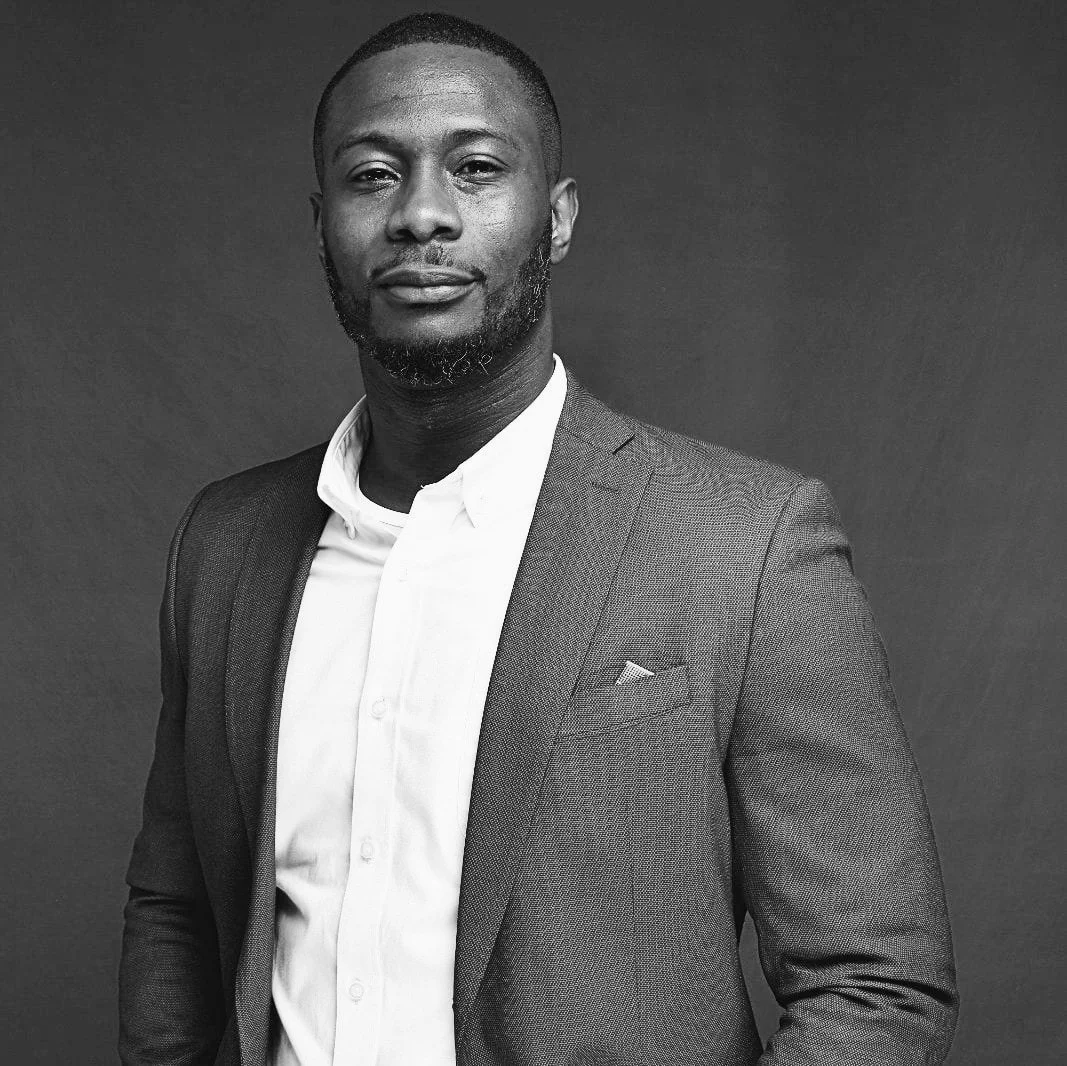 Portrait of a confident Black man in a suit against a dark background, in black and white.
