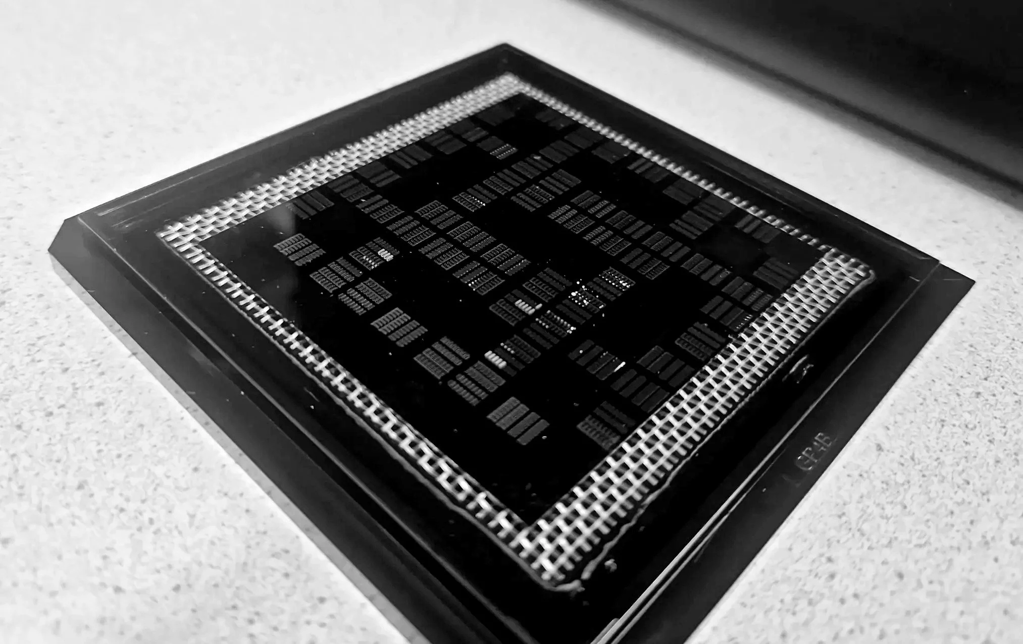 Black-and-white image of a computer processor chip with intricate circuitry, mounted on a black socket on a light-colored surface.