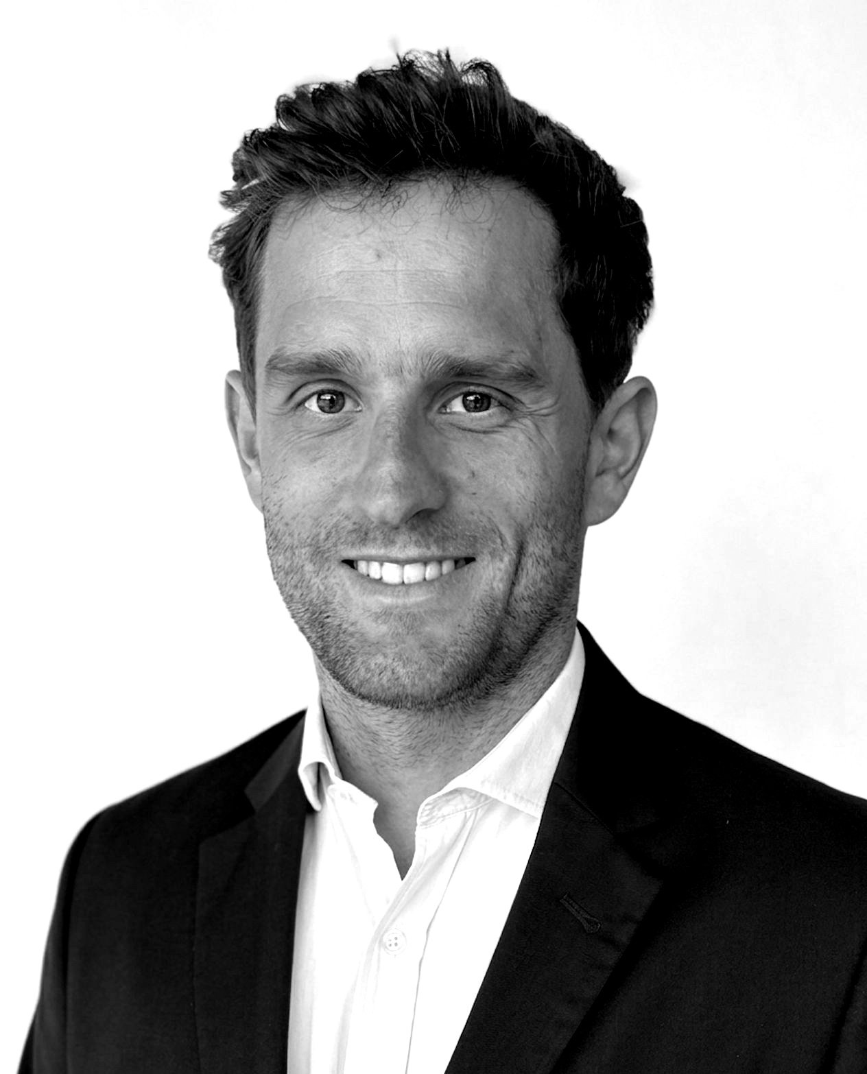 Black and white headshot of a smiling man wearing a suit and white shirt against a plain background.