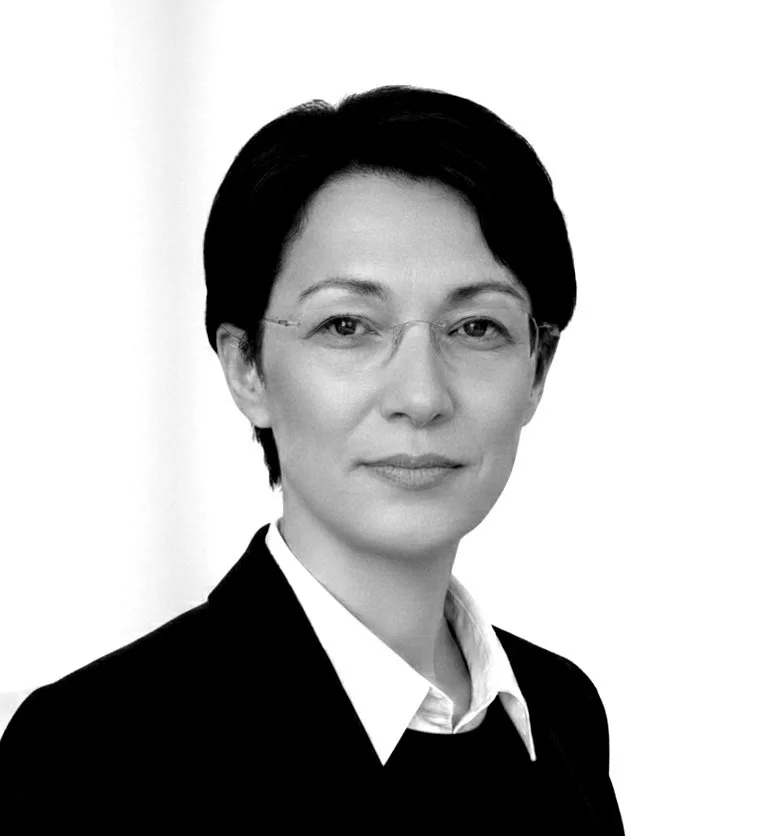 Black and white portrait of a woman with short dark hair wearing glasses, a white shirt, and a dark blazer.