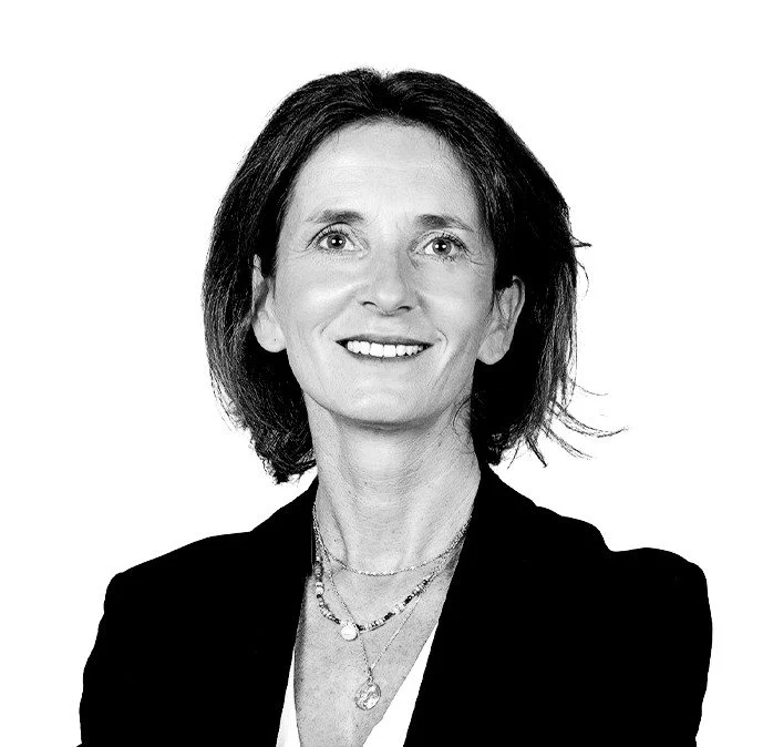 Black and white portrait of a smiling woman with shoulder-length dark hair, wearing a blazer and layered necklaces.