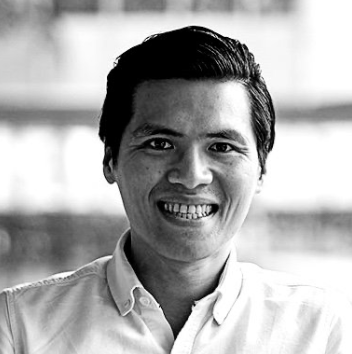 A smiling man with dark hair wearing a collared shirt in a grayscale photo.