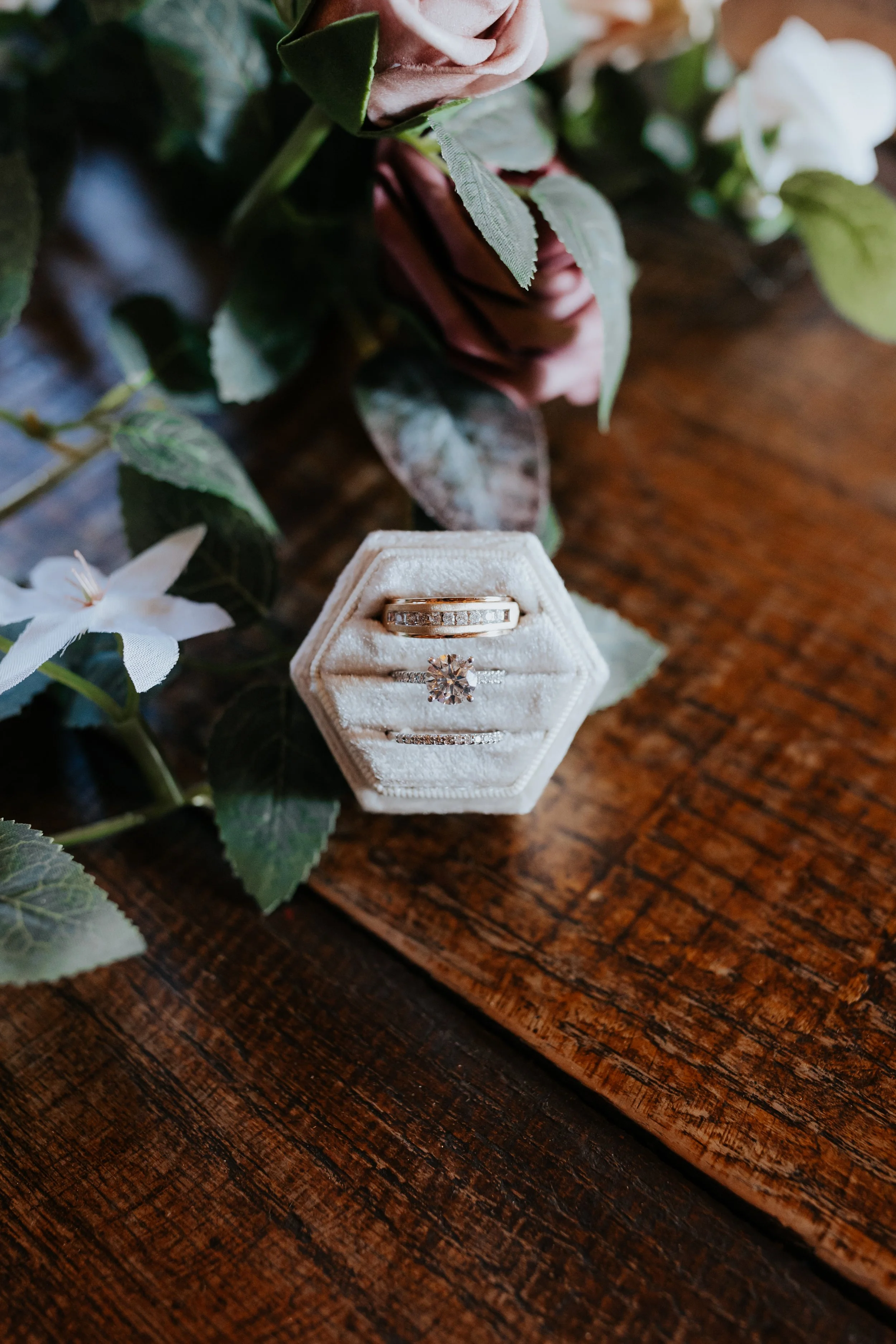 A hexagonal velvet ring box containing three rings, with a floral backdrop on a wooden surface.