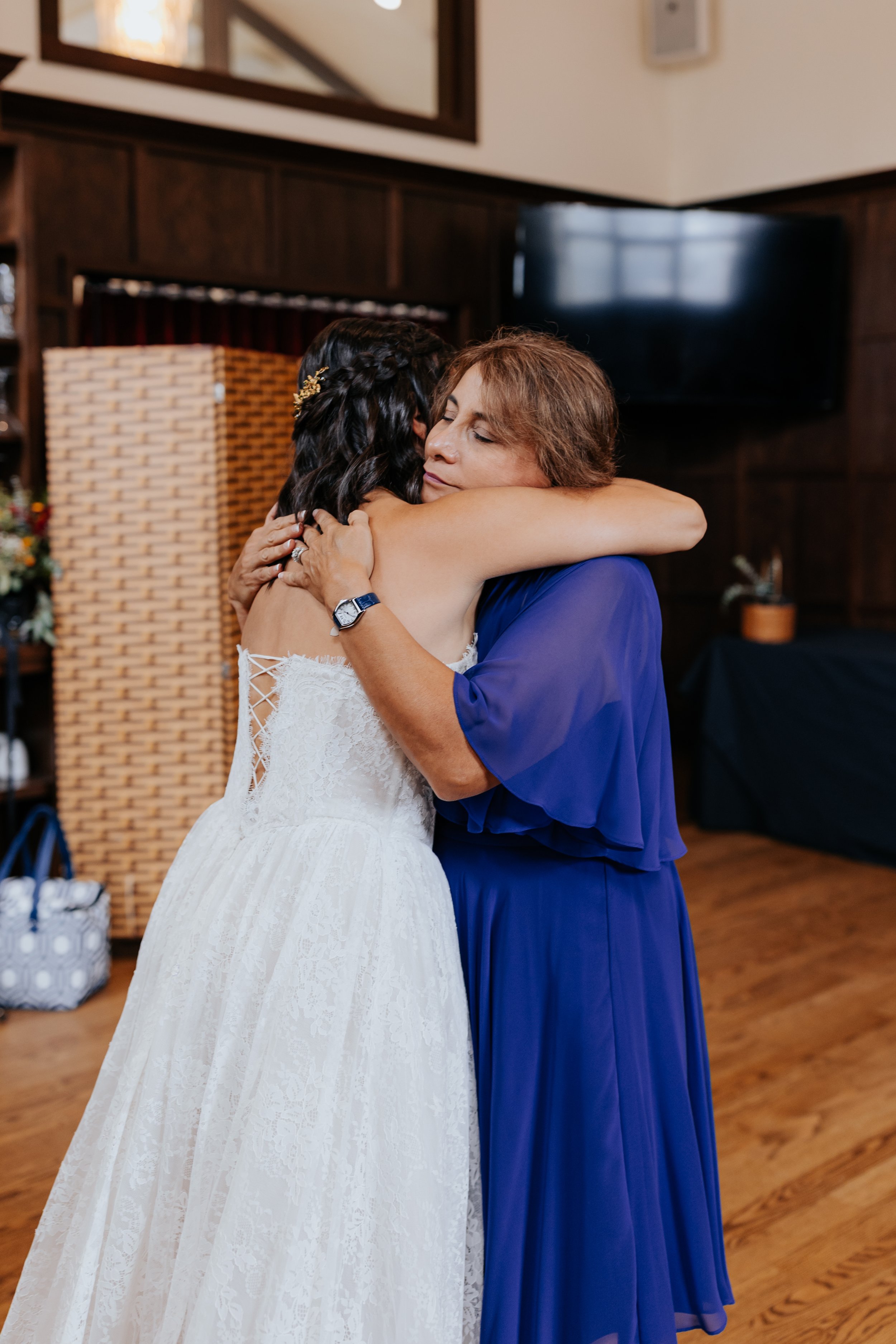A bride and an older woman hugging each other warmly in a room, likely during a wedding celebration.