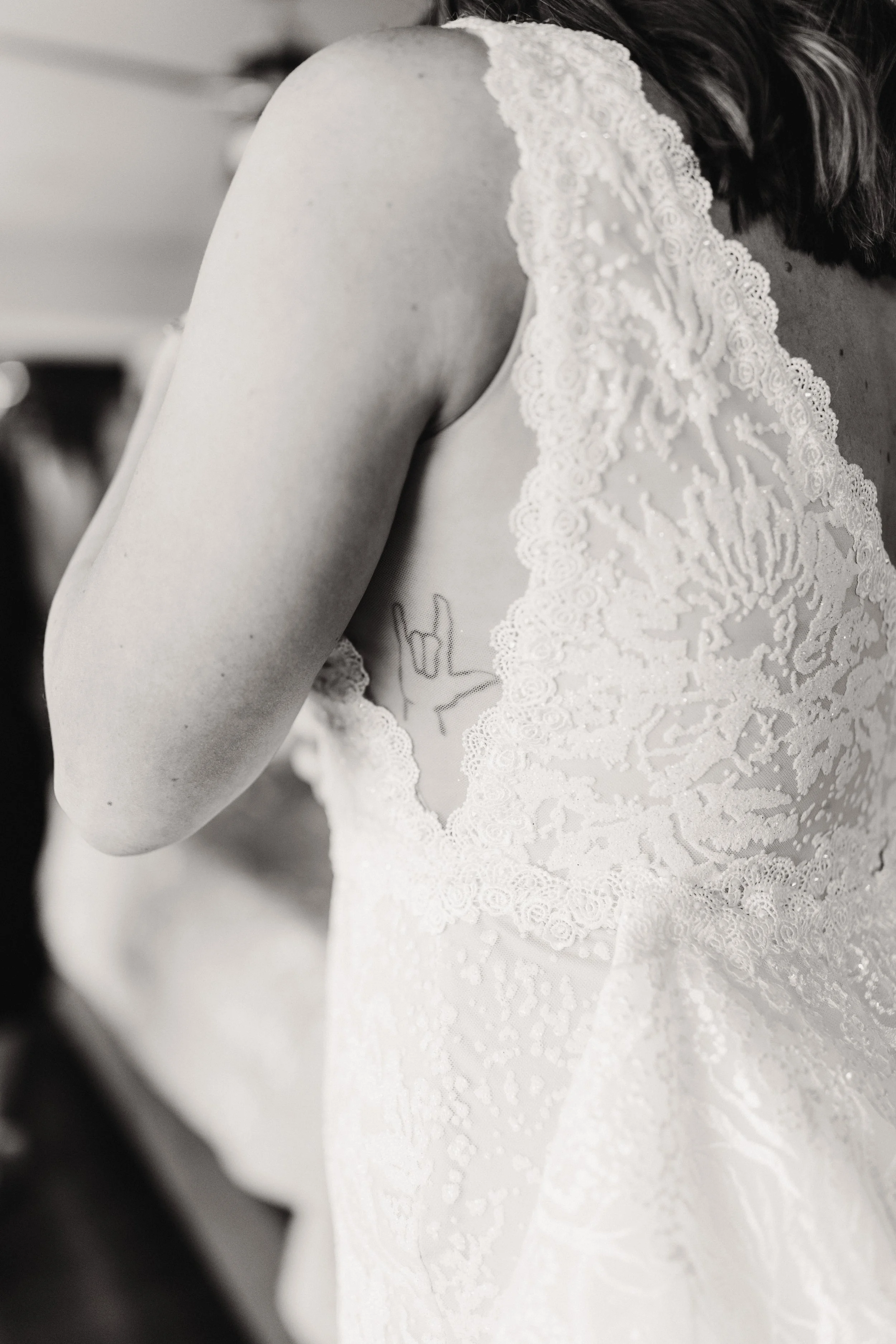 Close-up of a bride in a lace wedding dress with an exposed tattoo on her chest.