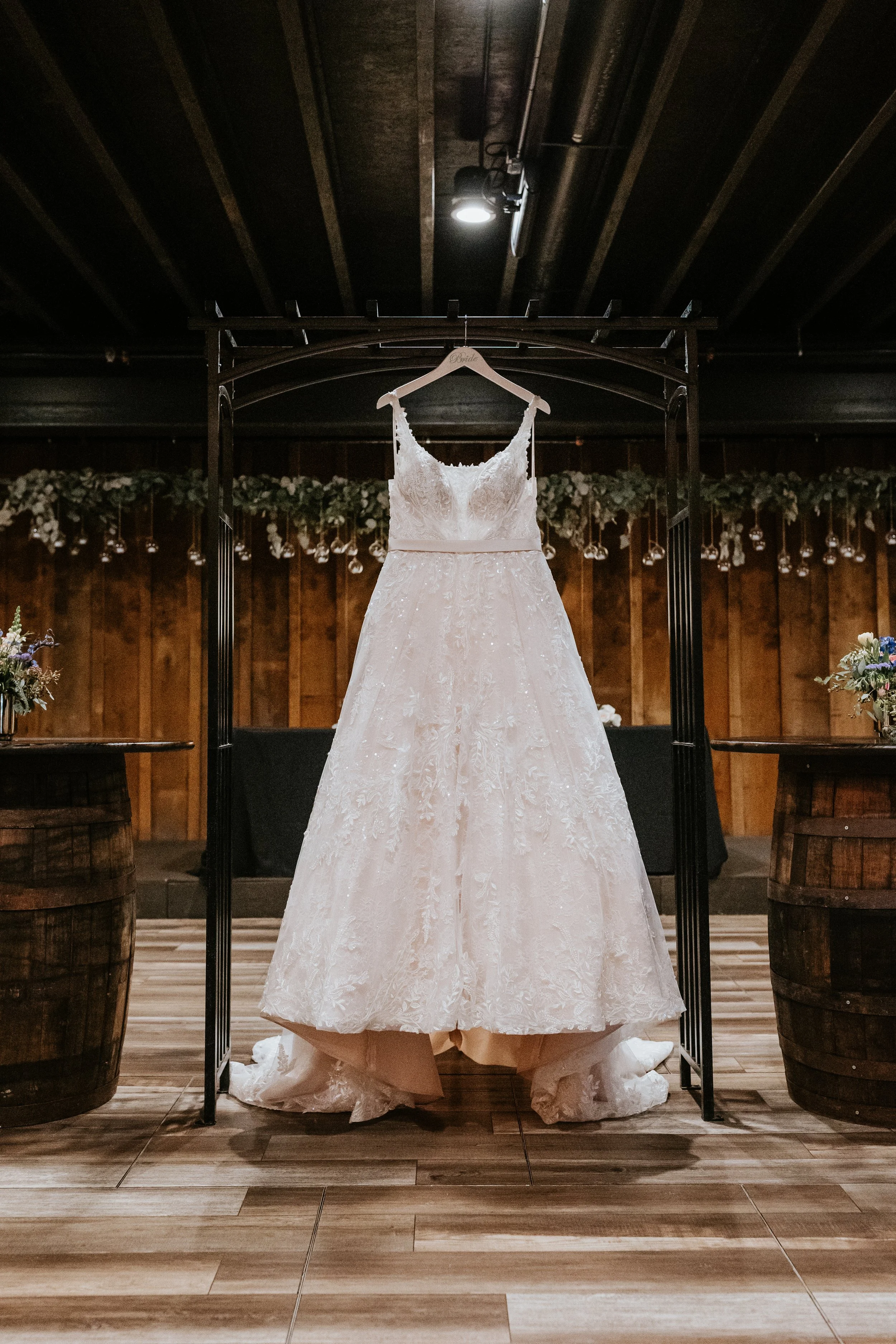 A wedding dress hanging on a rack in a rustic venue with wooden walls and floral decorations.