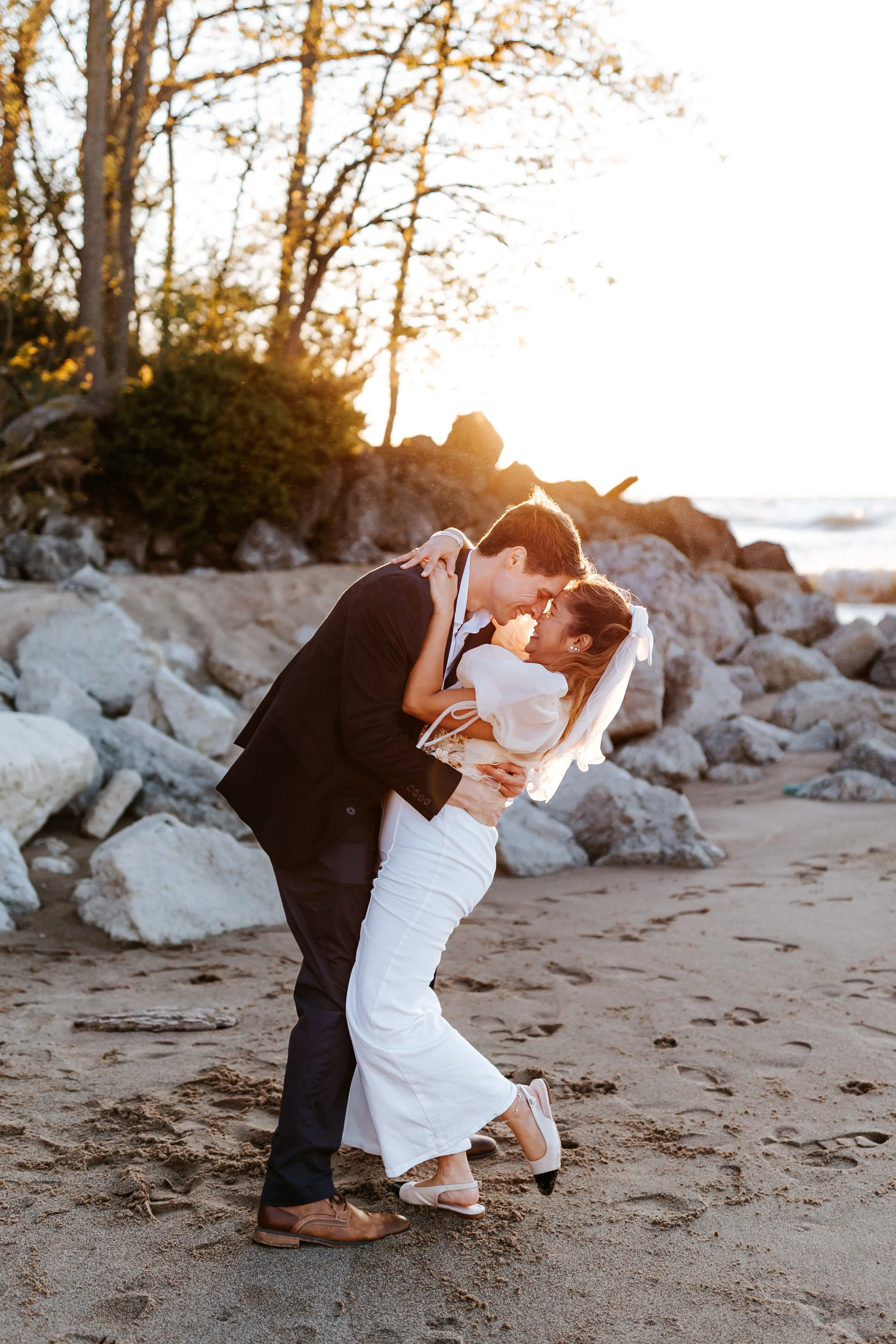 A couple dressed in wedding attire sharing an intimate moment on the beach at sunset.