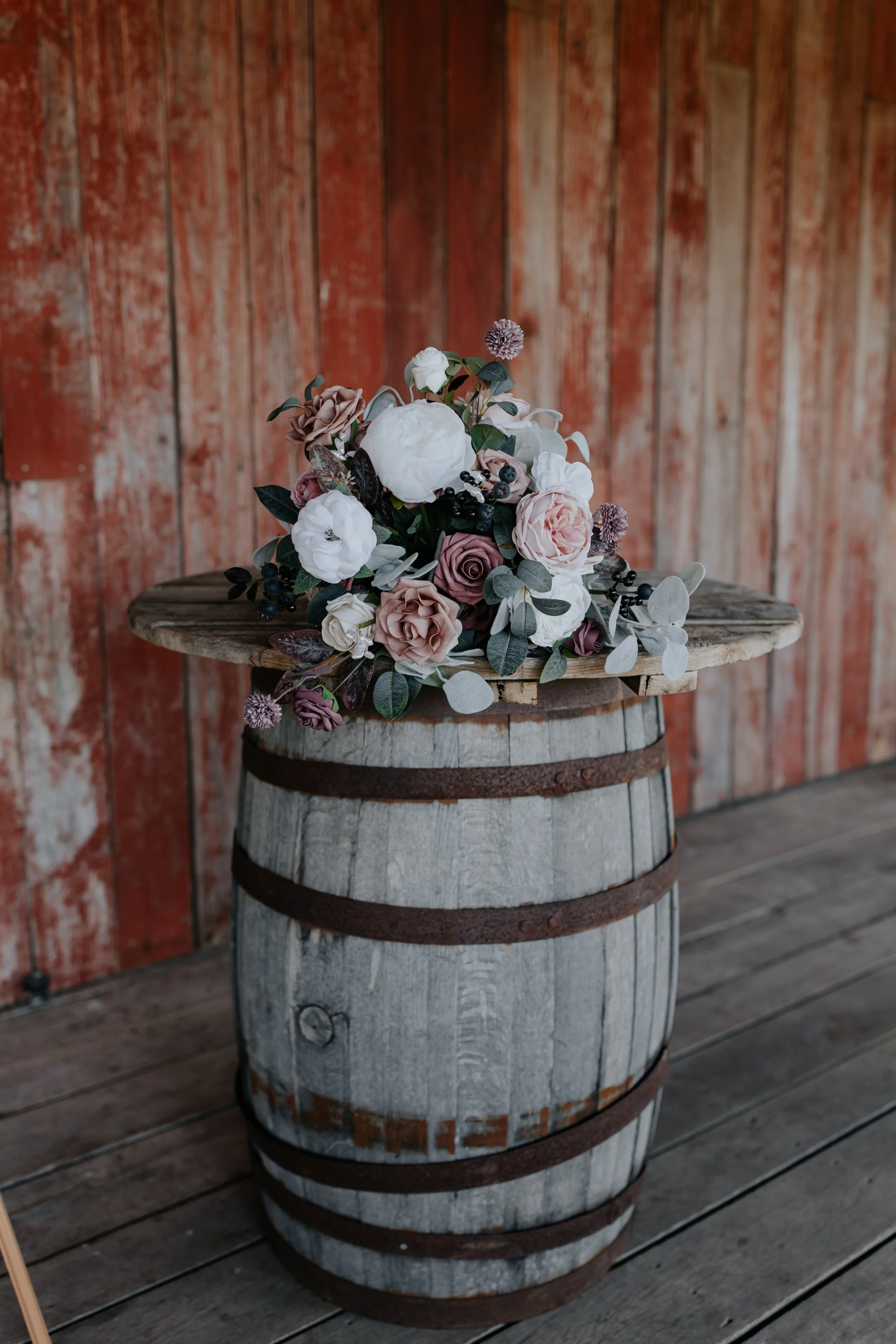 A bouquet of flowers resting on a rustic wooden barrel against a weathered red wooden wall.
