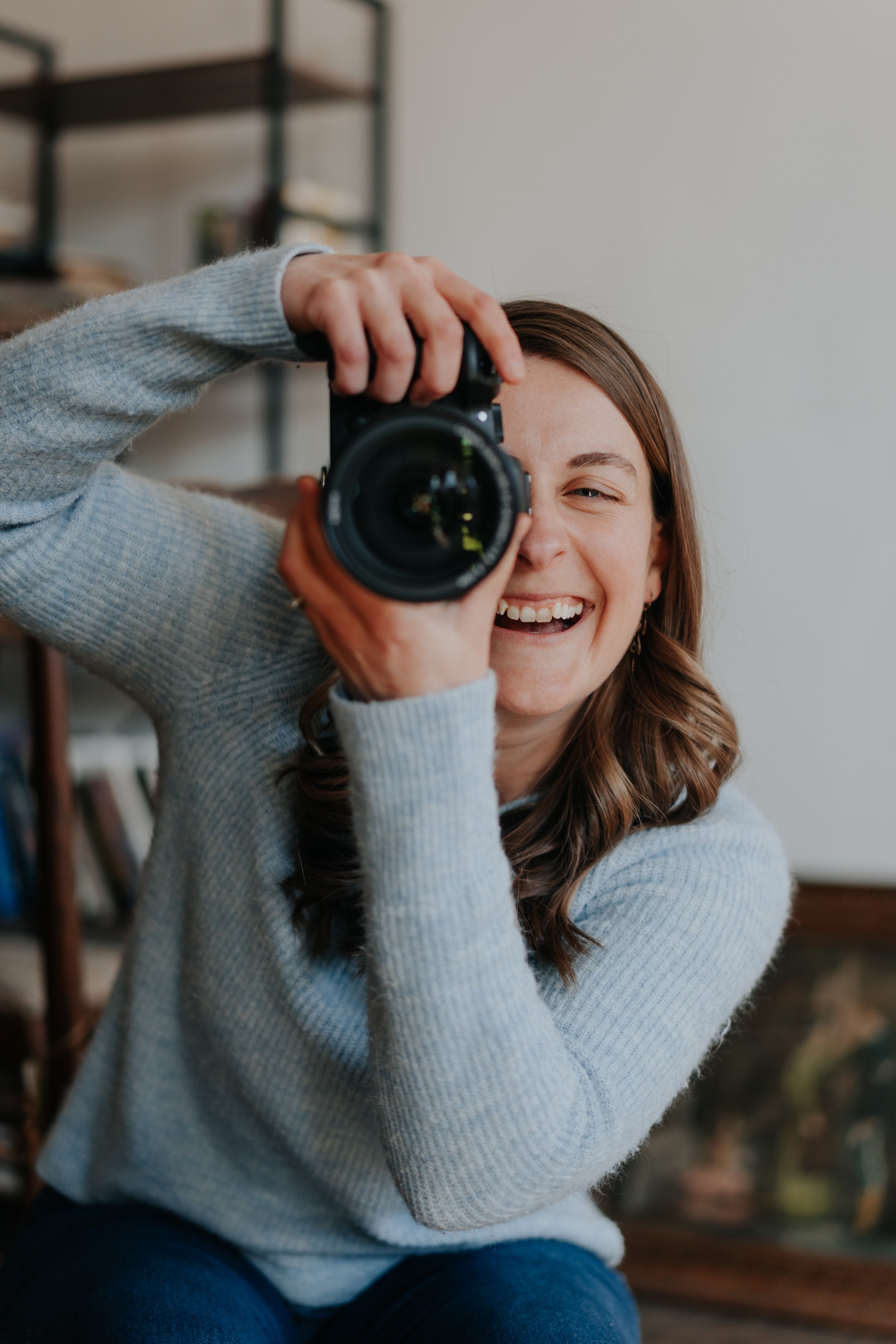 Smiling woman taking a photo with a camera indoors.