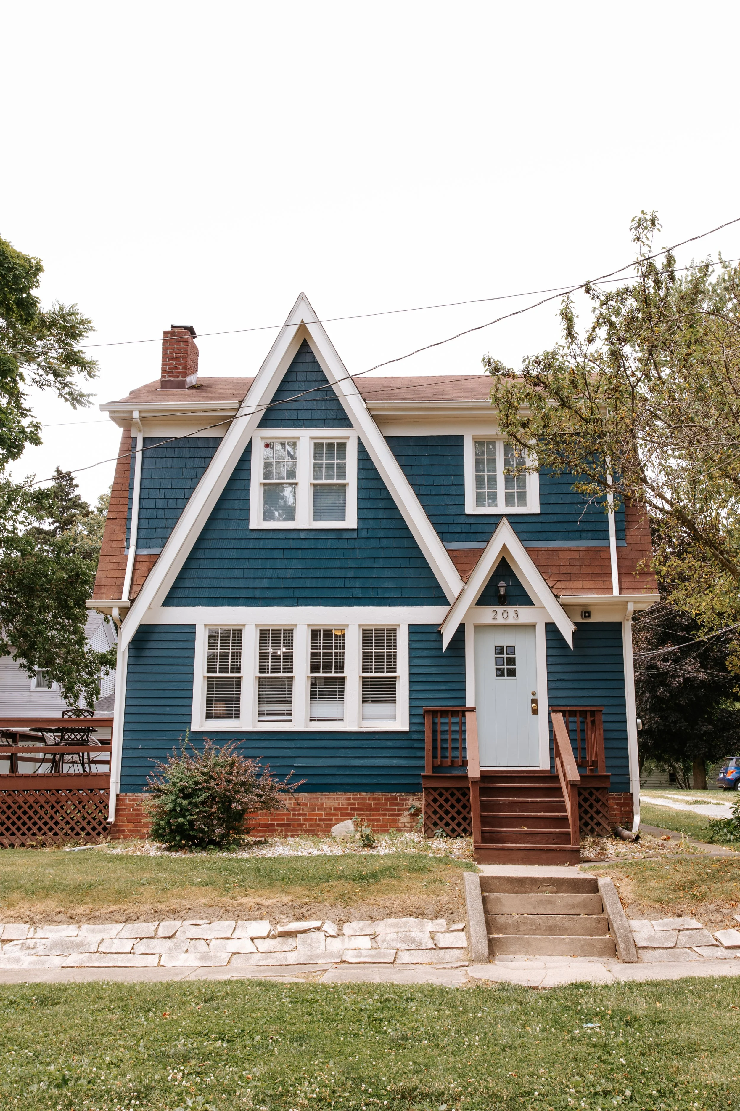 A blue house with white trim and a steep gable roof, featuring multiple windows and a small front porch.