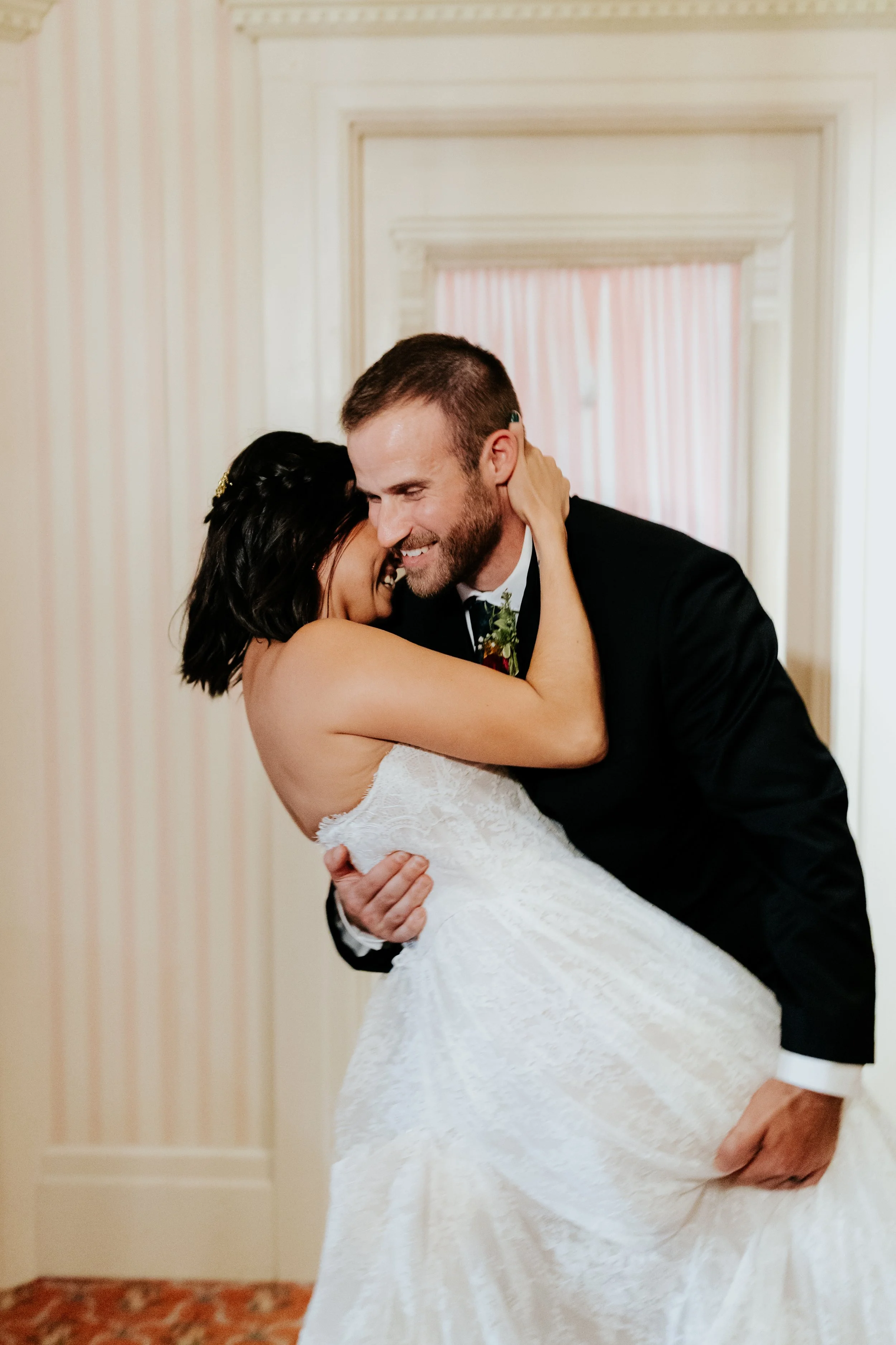A bride and groom sharing a joyful dance at their wedding in a decorated indoor venue.