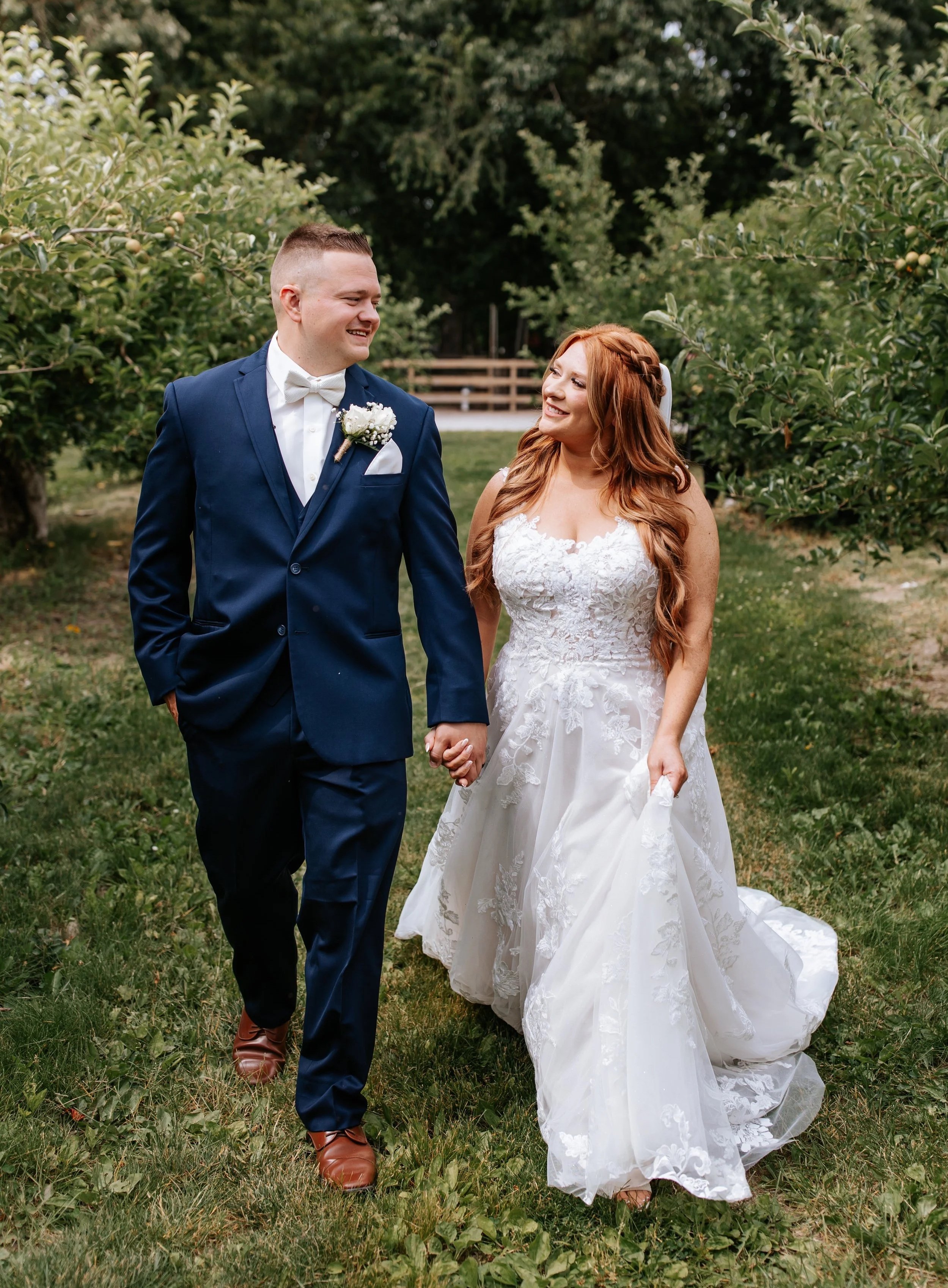 A newlywed couple walking hand in hand in an outdoor garden, smiling at each other.