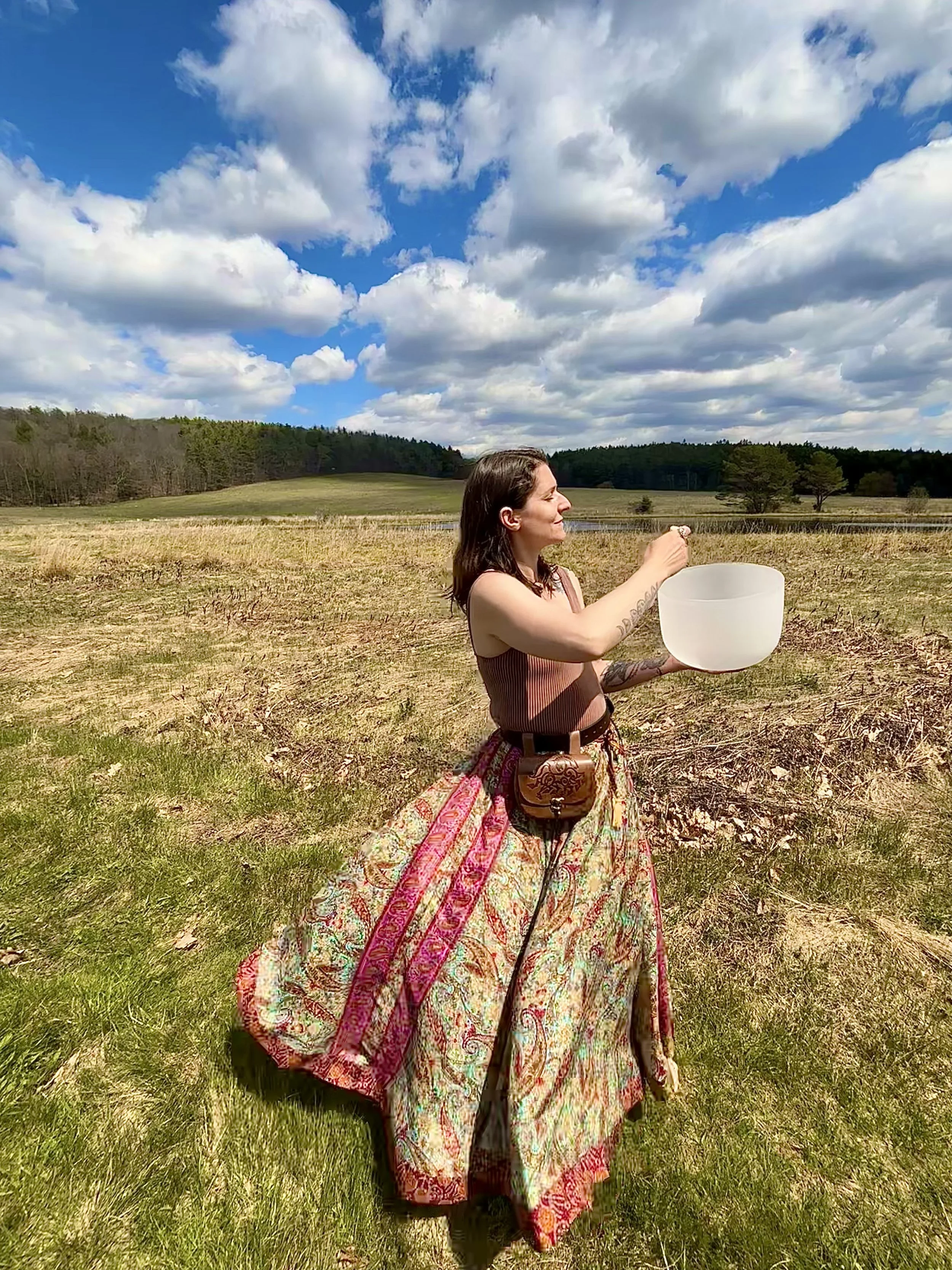 A woman holding a white bowl in a grassy field under a partly cloudy sky.