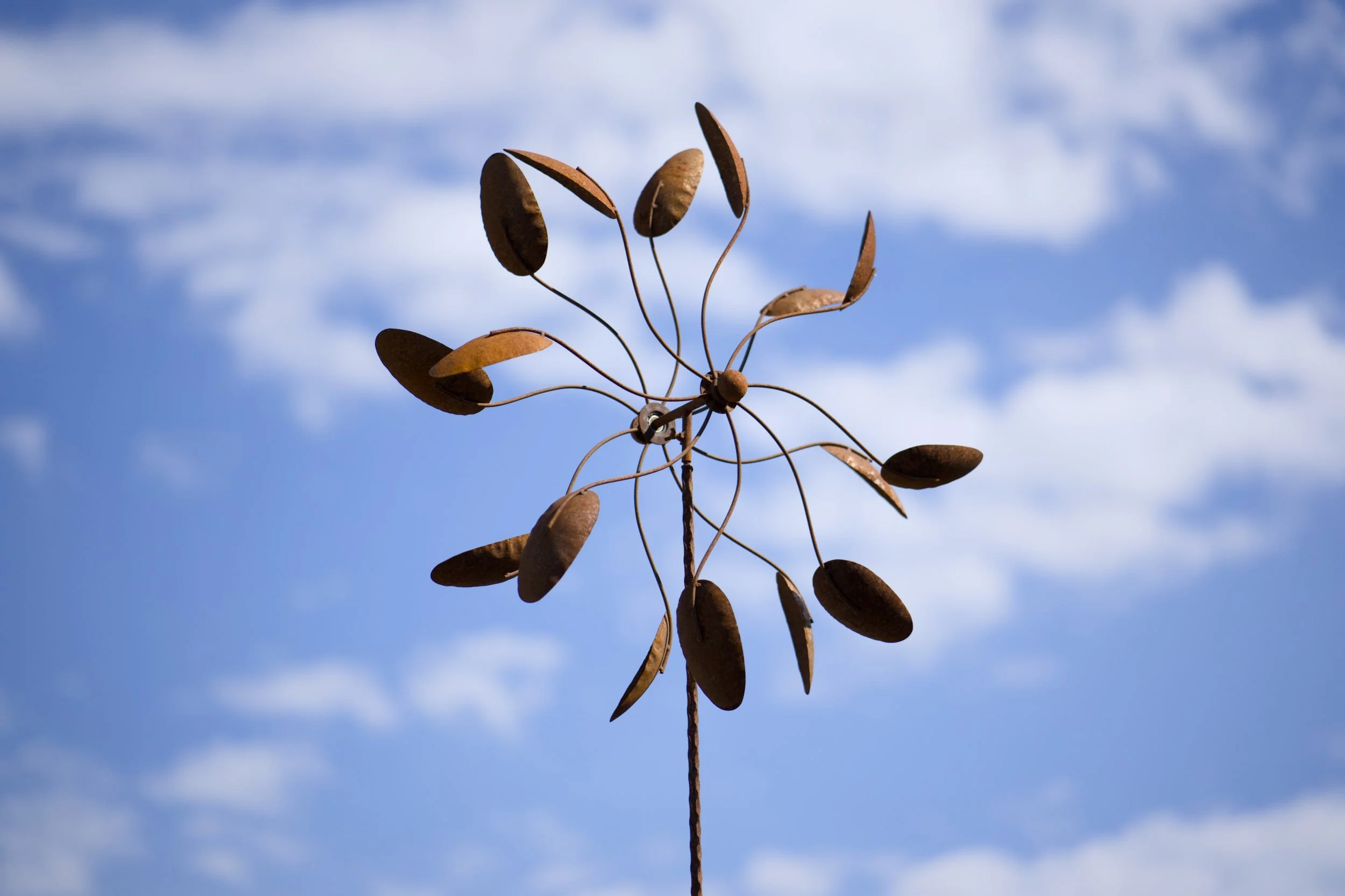 Eine metallische Skulptur mit mehreren ohrförmigen Elementen, die an dünnen Spiralen befestigt sind, vor einem blauen Himmel mit Wolken.
