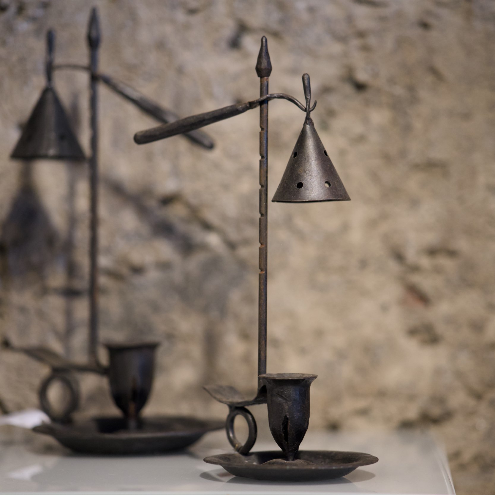 Metallene Kerzenhalter mit spiralförmigen und spitzen Dekorationen vor einer rauen Steinwand.