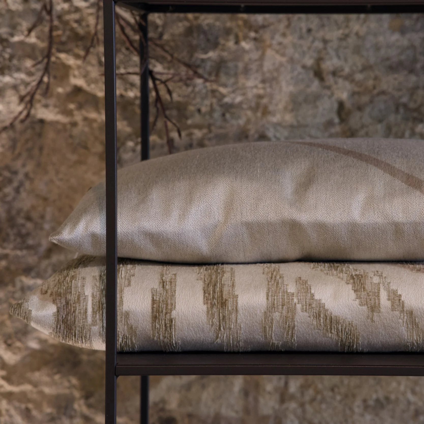 Zwei dekorative Kissen auf einer mehrstufigen, beige Couch, vor einem steinernen Hintergrund.