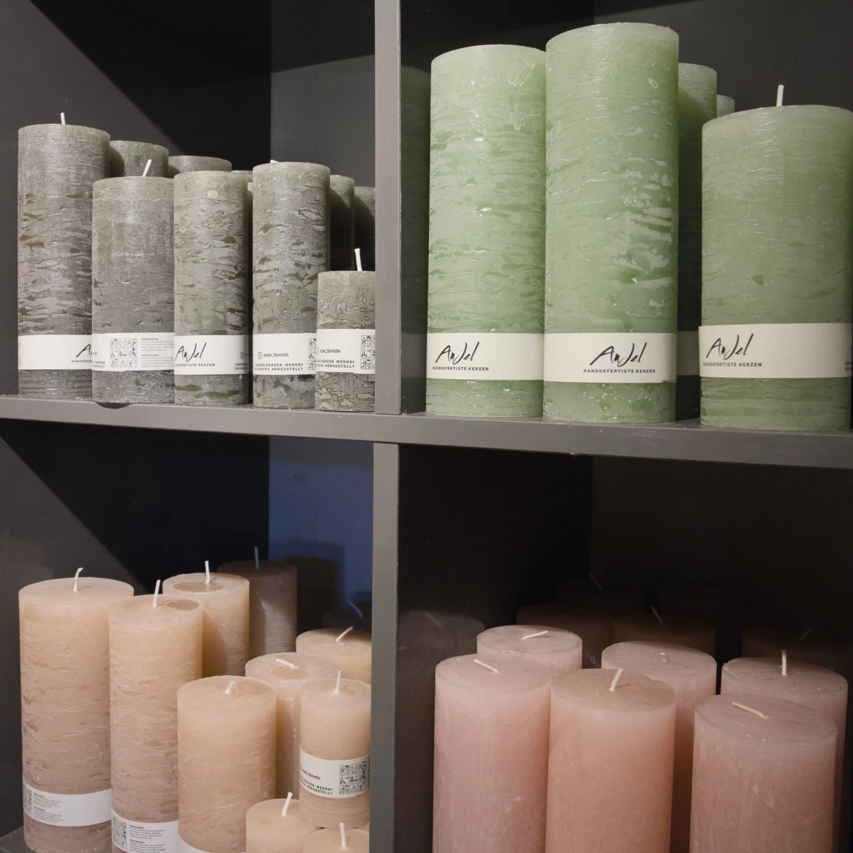 Verschiedene große Kerzen in verschiedenen Farben, grau, grün und pfirsich auf einer schwarzen Regalfläche.